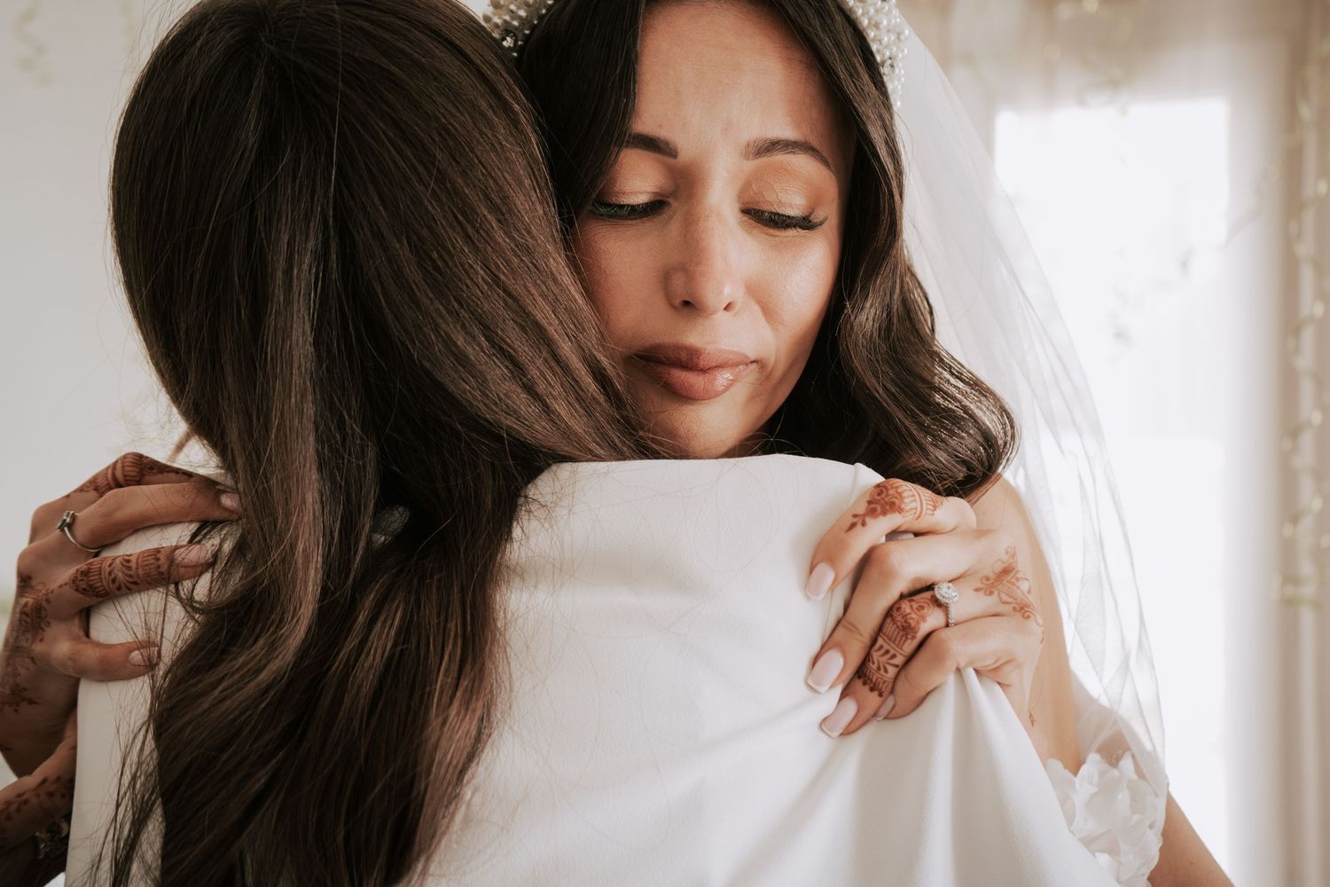 Emotional mother embraces her daughter in a white wedding dress in a heartfelt pre-wedding moment.
