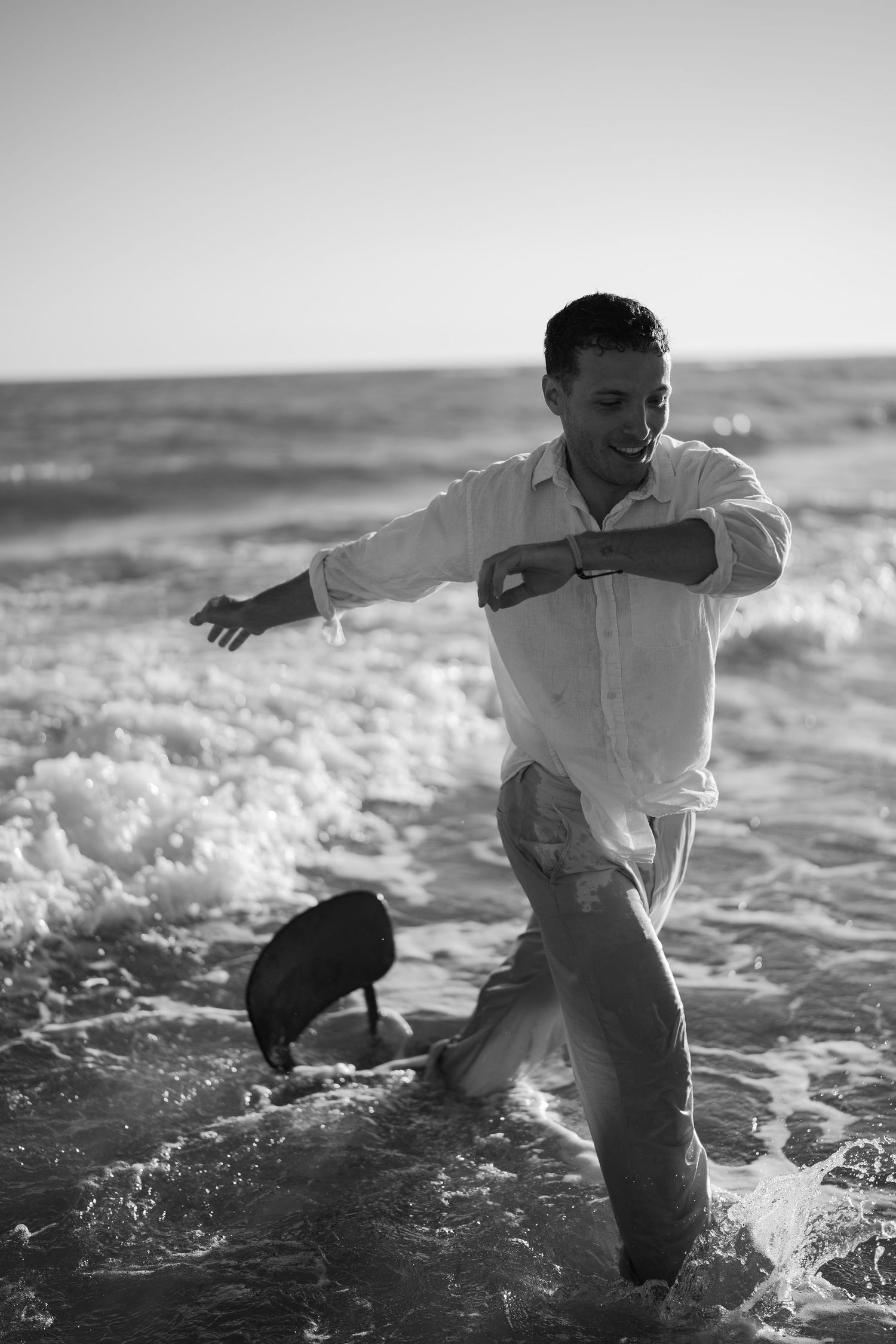 Joyful man in white shirt playing in ocean waves with chair on beach, black and white photo.