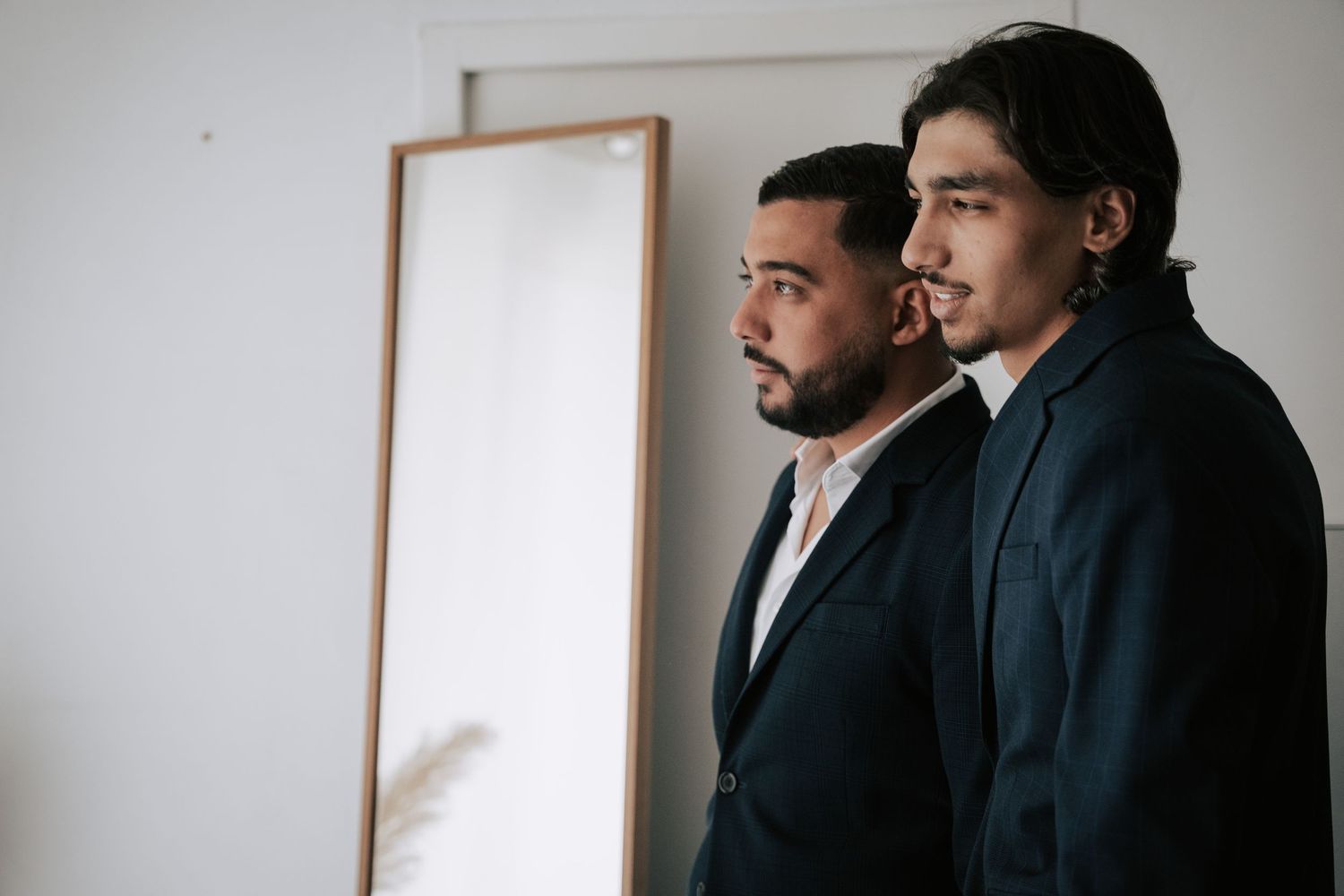 Two men in dark suits stand together looking thoughtfully in a bright modern room.