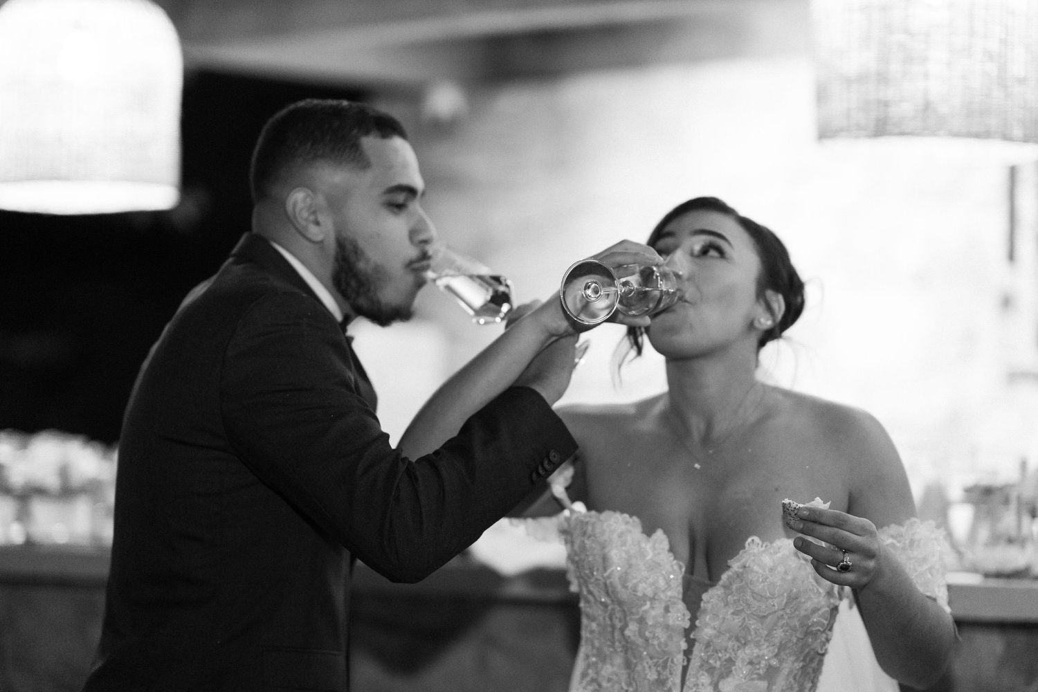 Black and white photo of bride and groom doing a wedding toast, drinking champagne together at their reception.