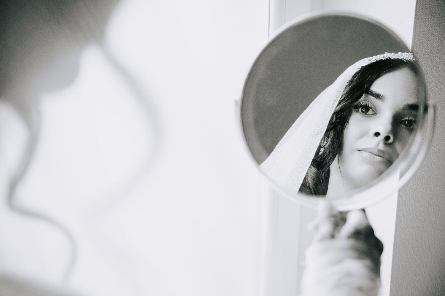 Black and white portrait of bride in veil reflected in a round mirror on wedding day.