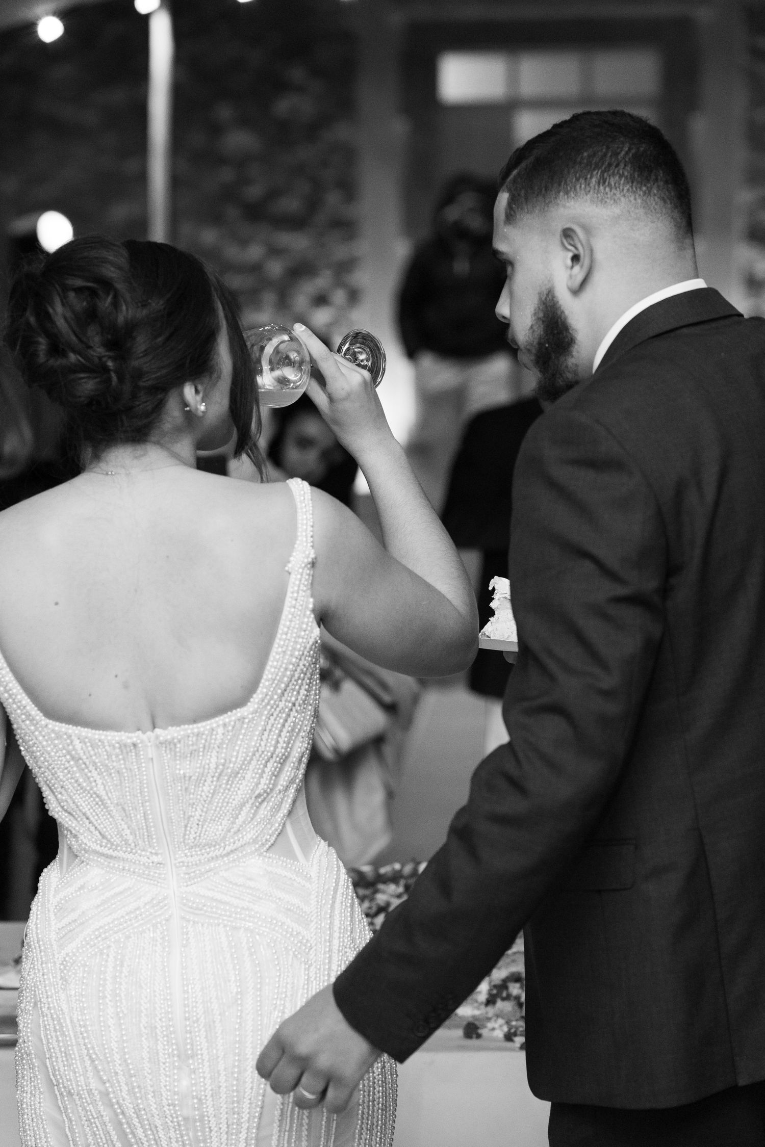 Black and white photo of bride and groom holding hands and raising champagne glasses at their wedding reception.