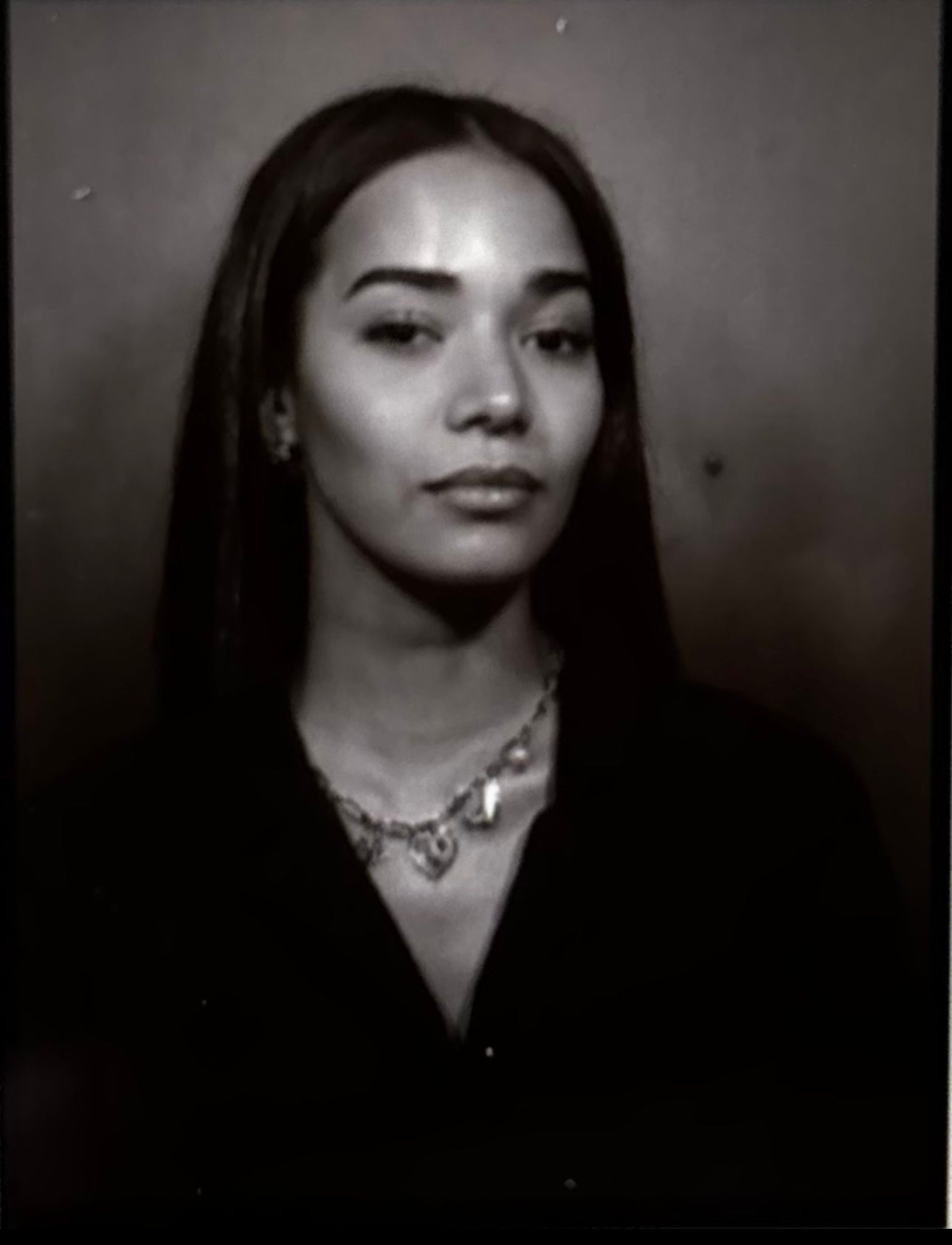 Black and white portrait photo of a young woman with long hair wearing a chain necklace and dark top.