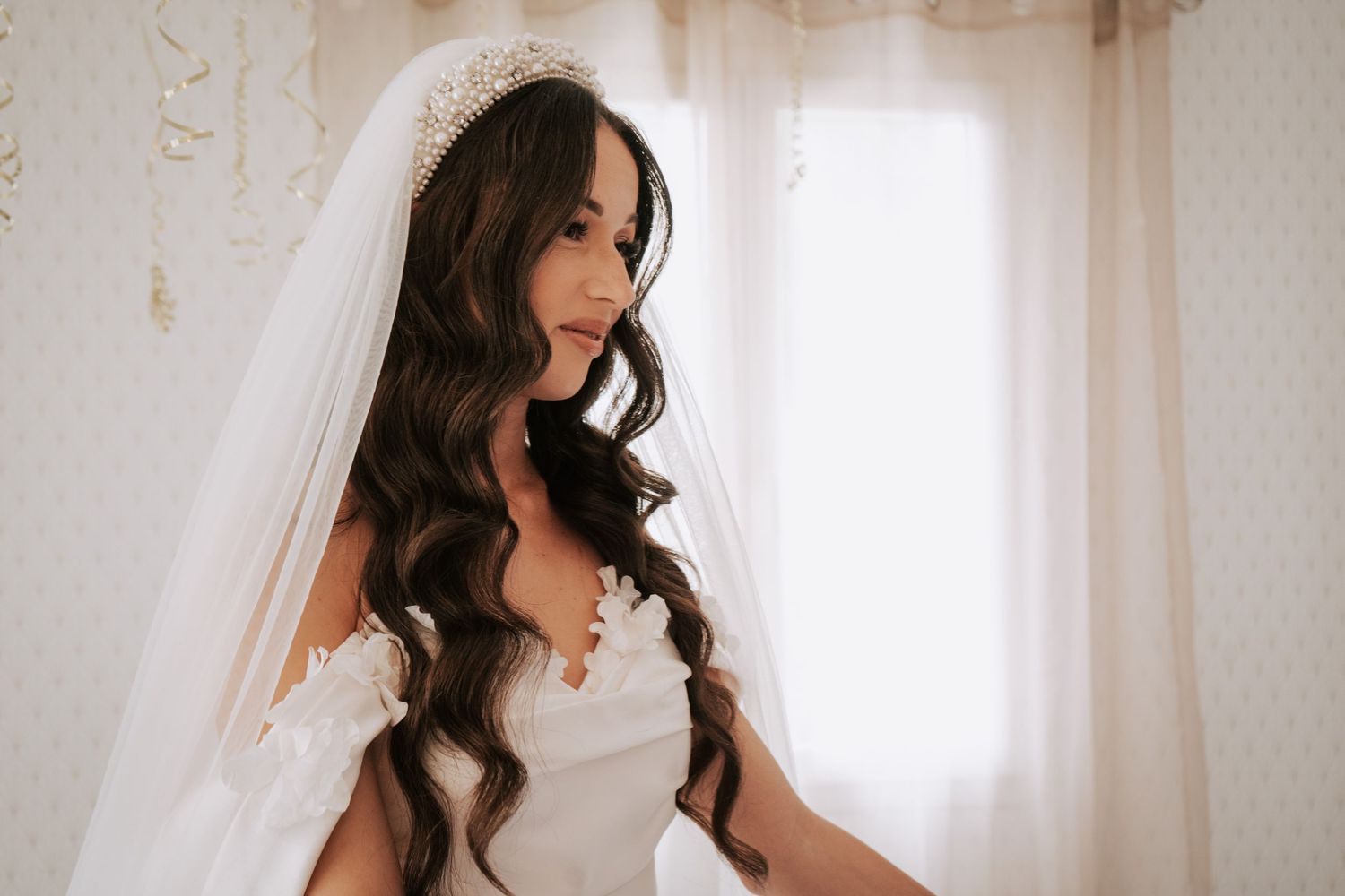 Elegant bride with long wavy hair wearing a white wedding gown and veil with a crystal tiara.