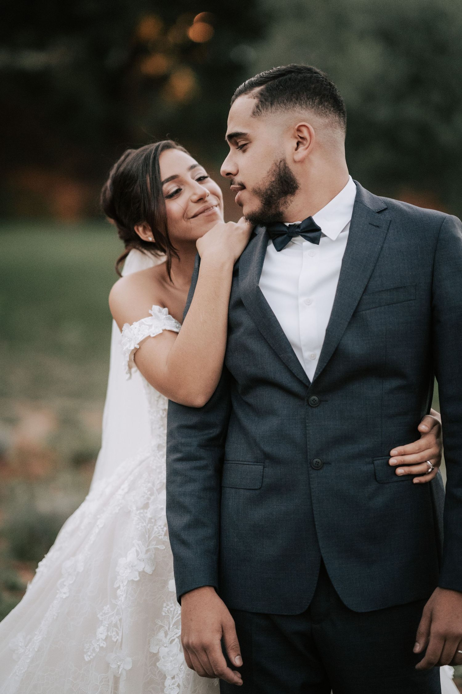 Bride tenderly touches grooms face as they share an intimate moment in elegant wedding attire outdoors.