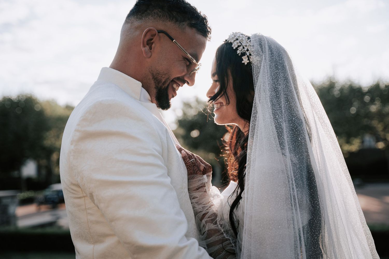 Bride and groom share an intimate moment, smiling face to face in soft outdoor light.