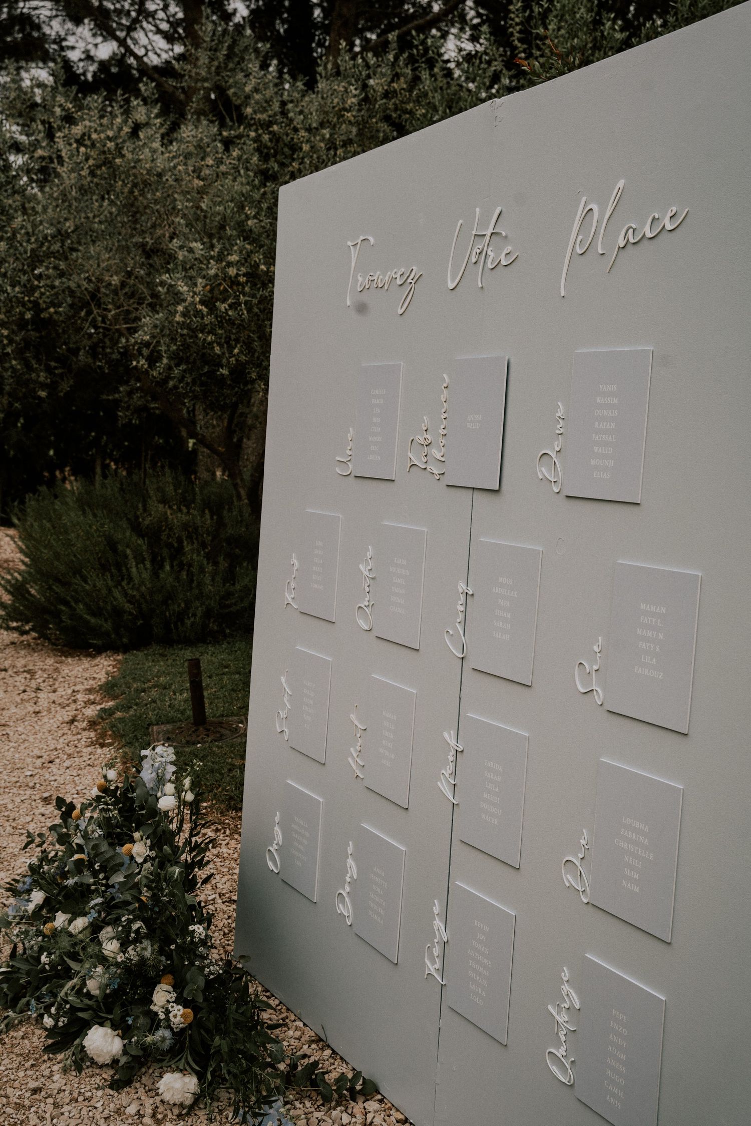 Sage green seating chart display with white script lettering and floral accents in garden.