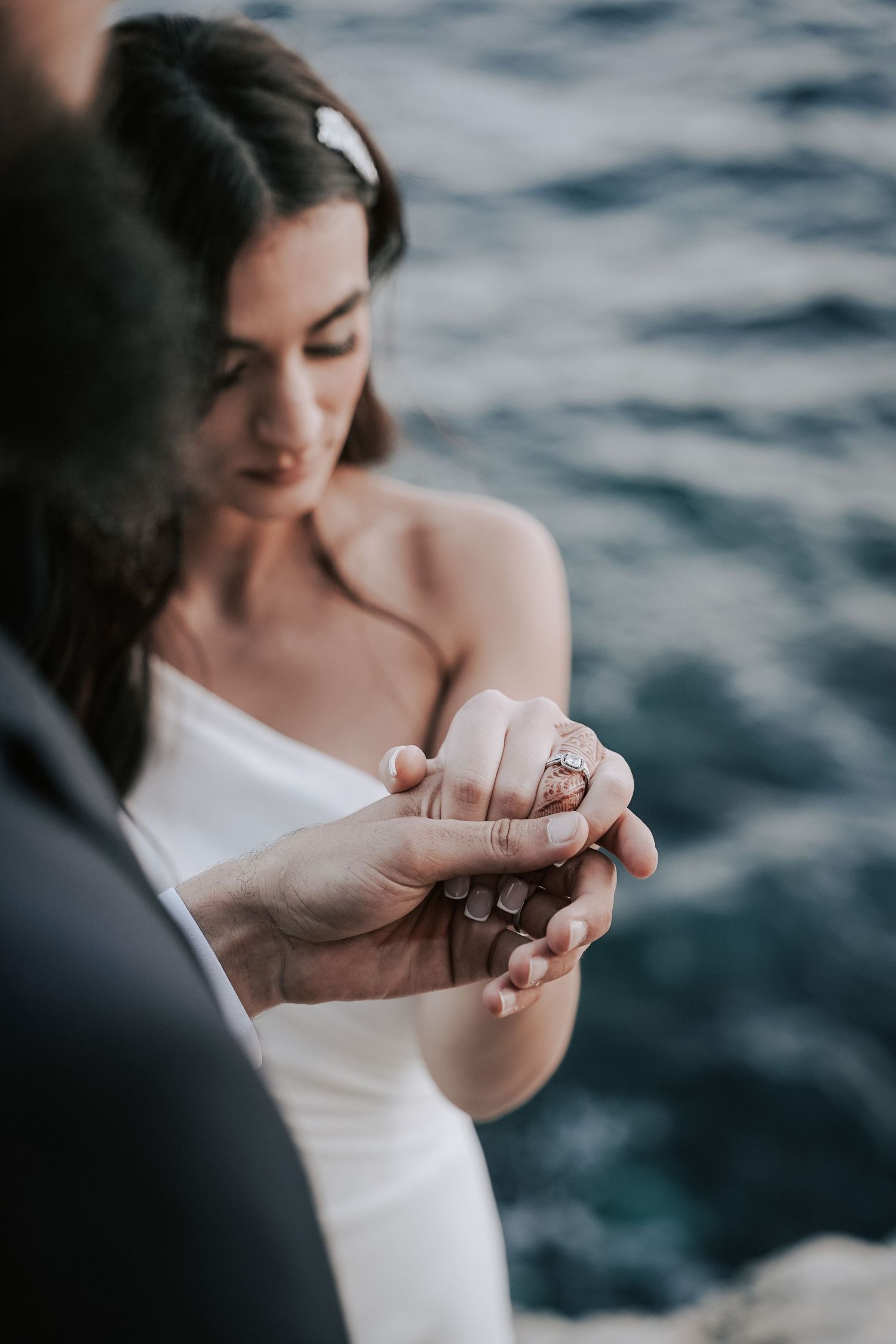 Bride and groom tenderly holding hands near the ocean at their seaside wedding ceremony.