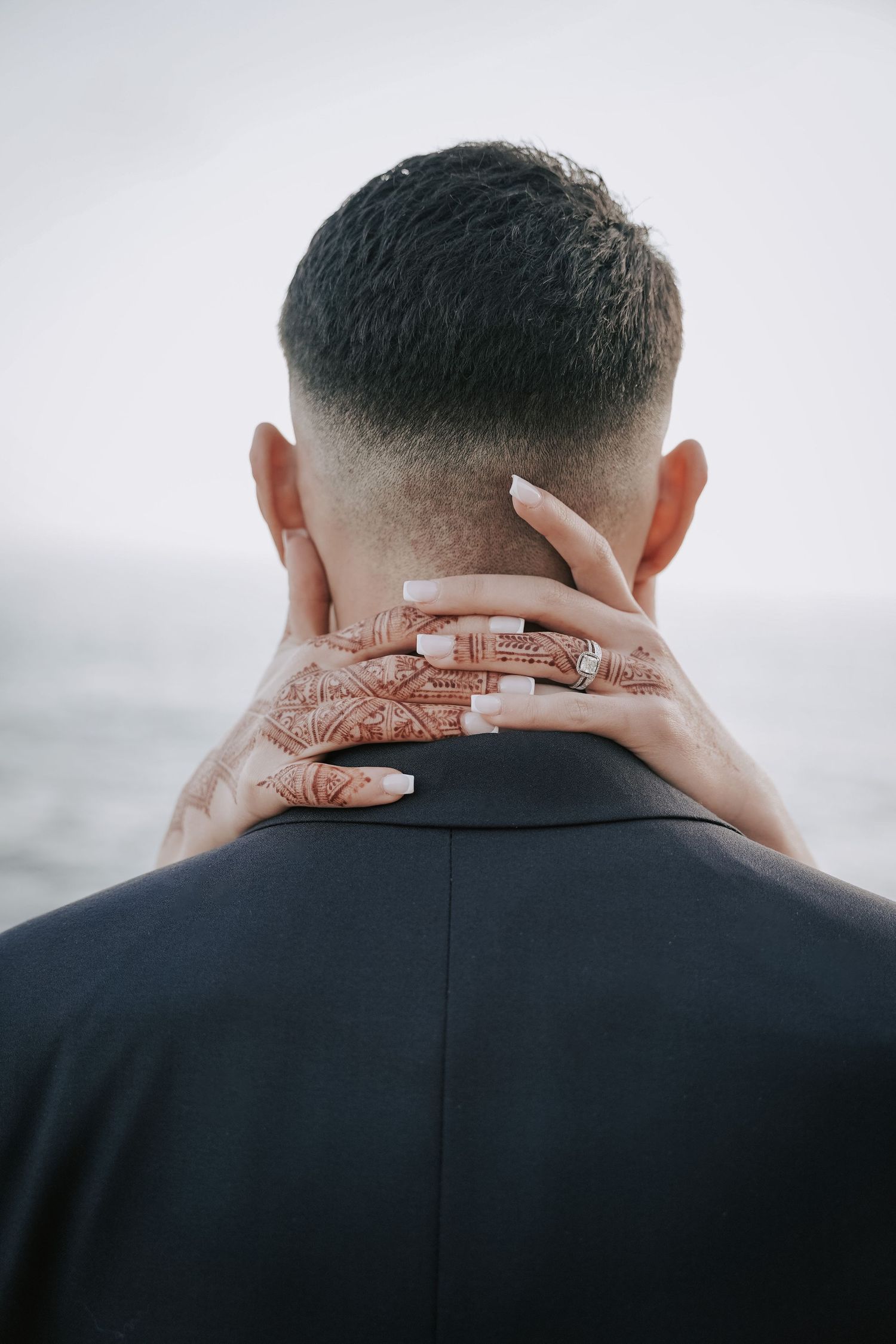 Bride with henna tattoo hand gently placed on grooms neck at outdoor seaside wedding.
