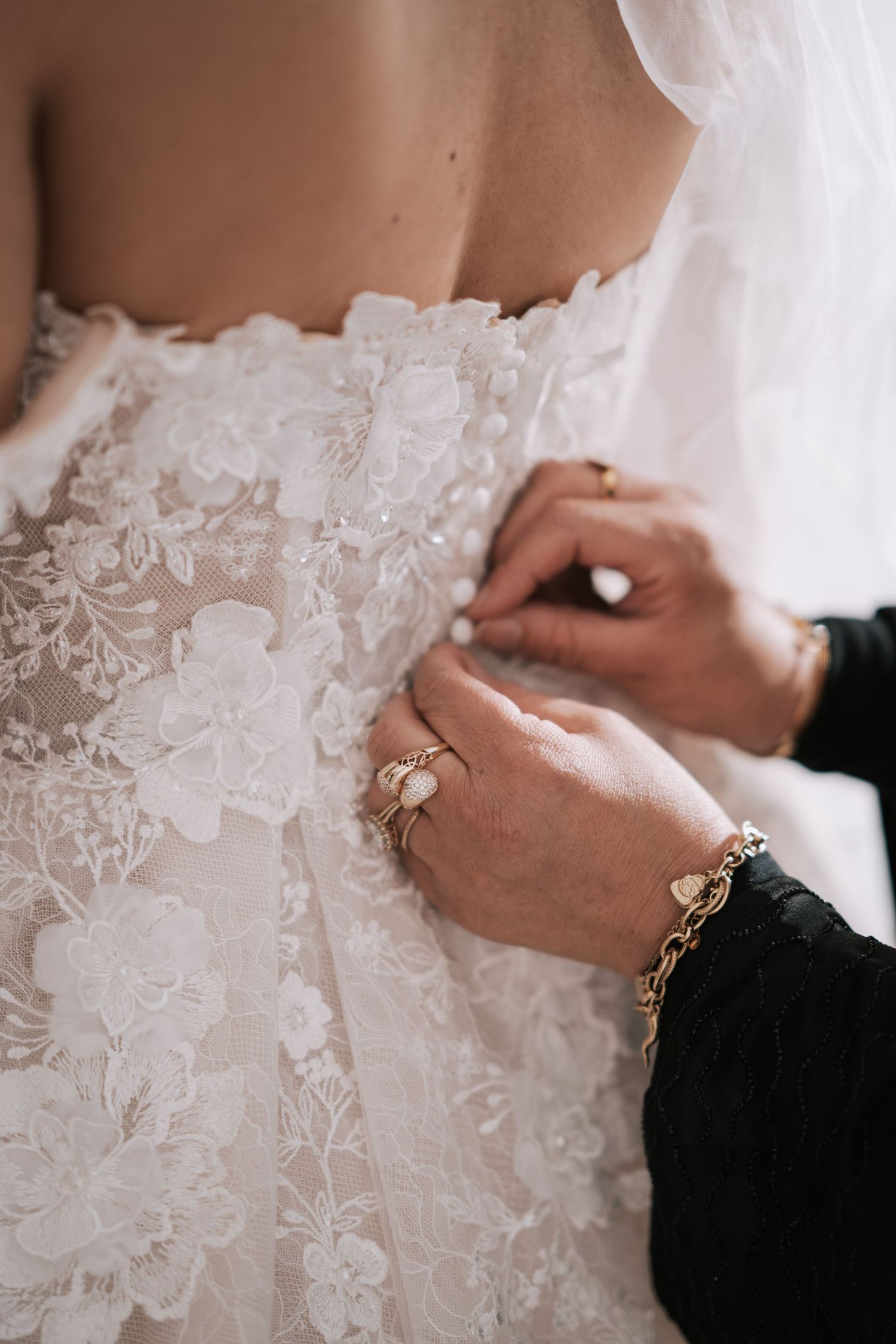 Close-up of hands fastening delicate buttons on intricate floral lace wedding dress back.