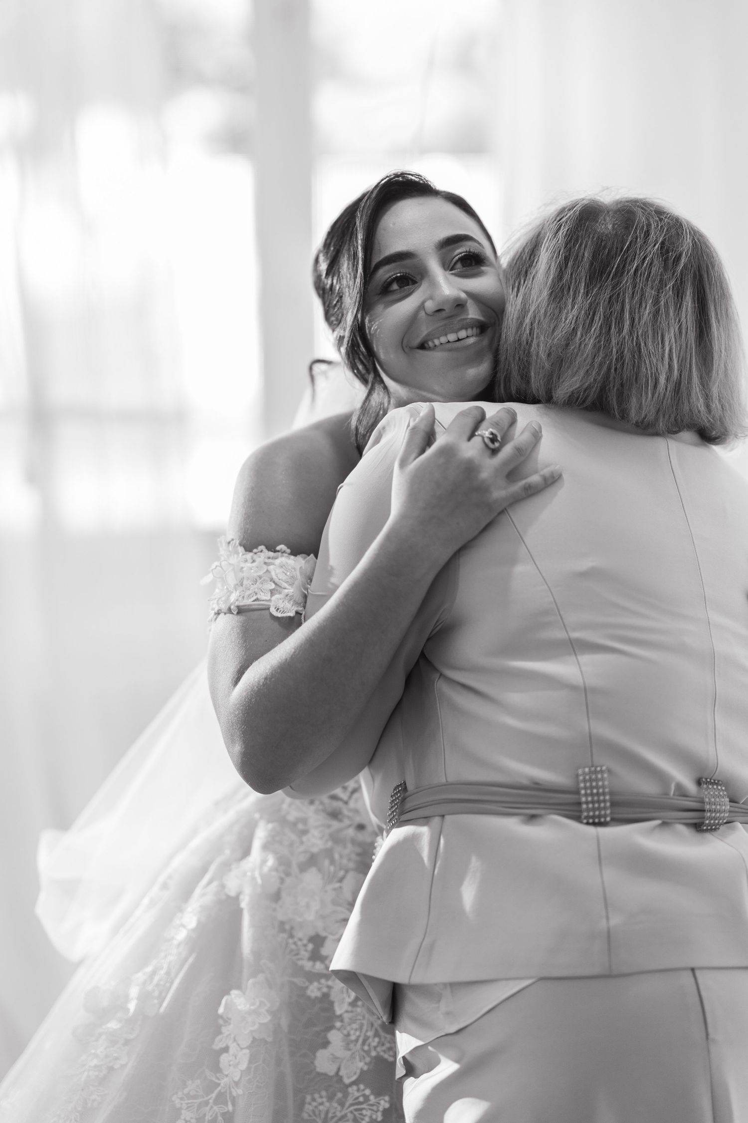 Smiling bride in lace wedding dress sharing tender hug in black and white photo.