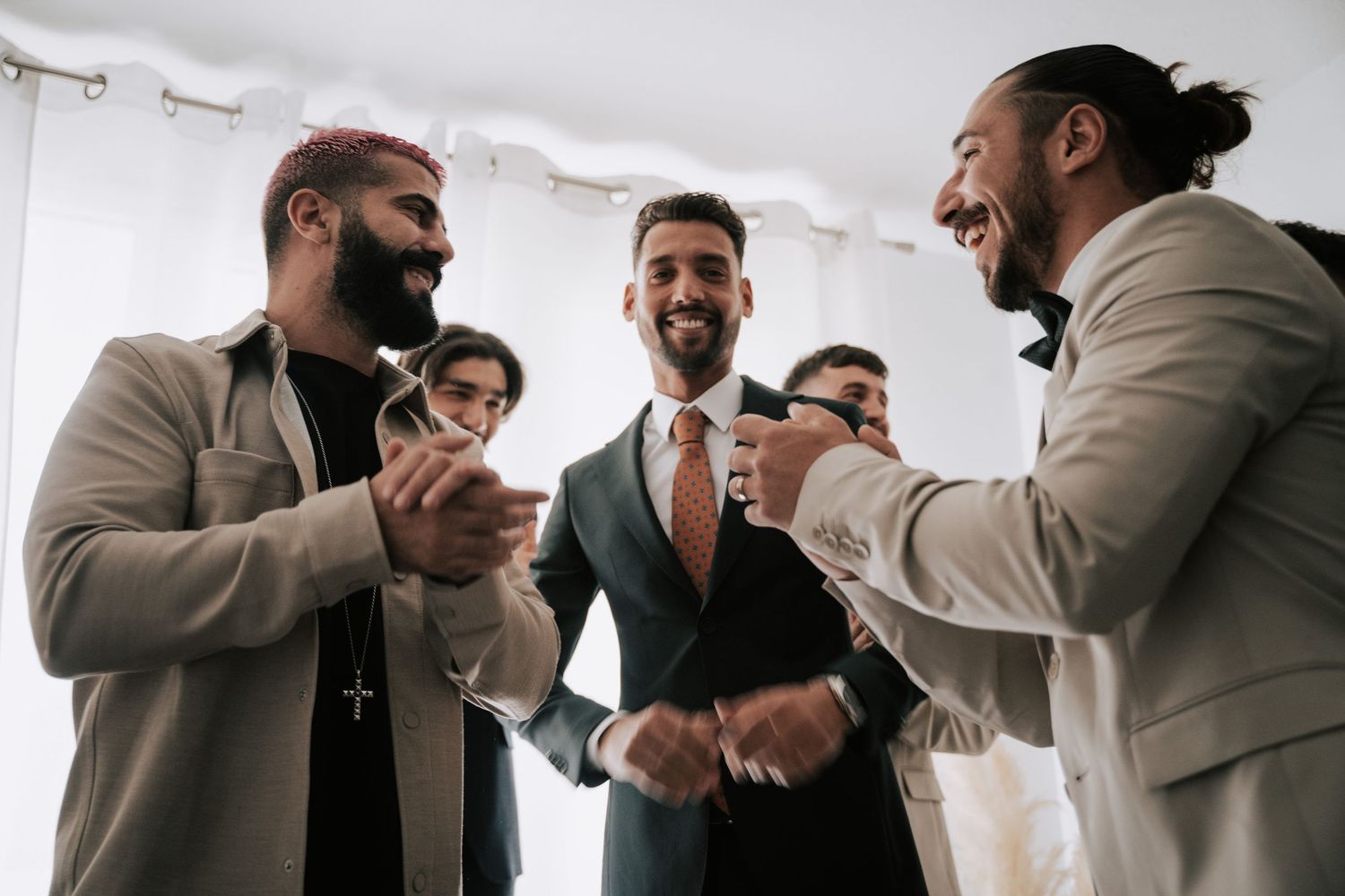 Groomsmen laughing and celebrating together before a wedding ceremony in stylish suits.