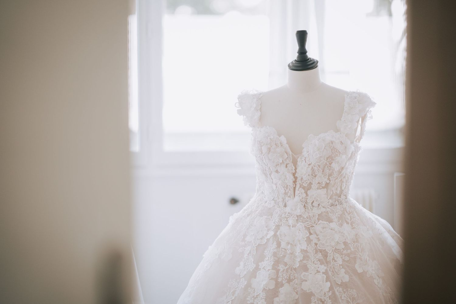 Stunning floral lace wedding gown displayed on a mannequin near a bright window.