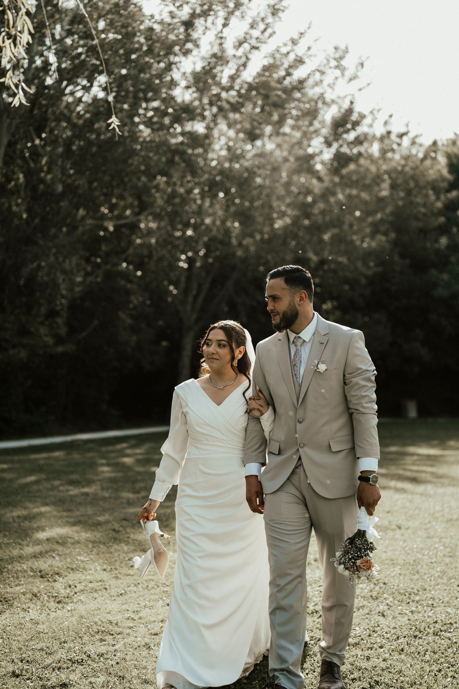 Bride and groom walking arm in arm through a golden-lit garden on their wedding day.