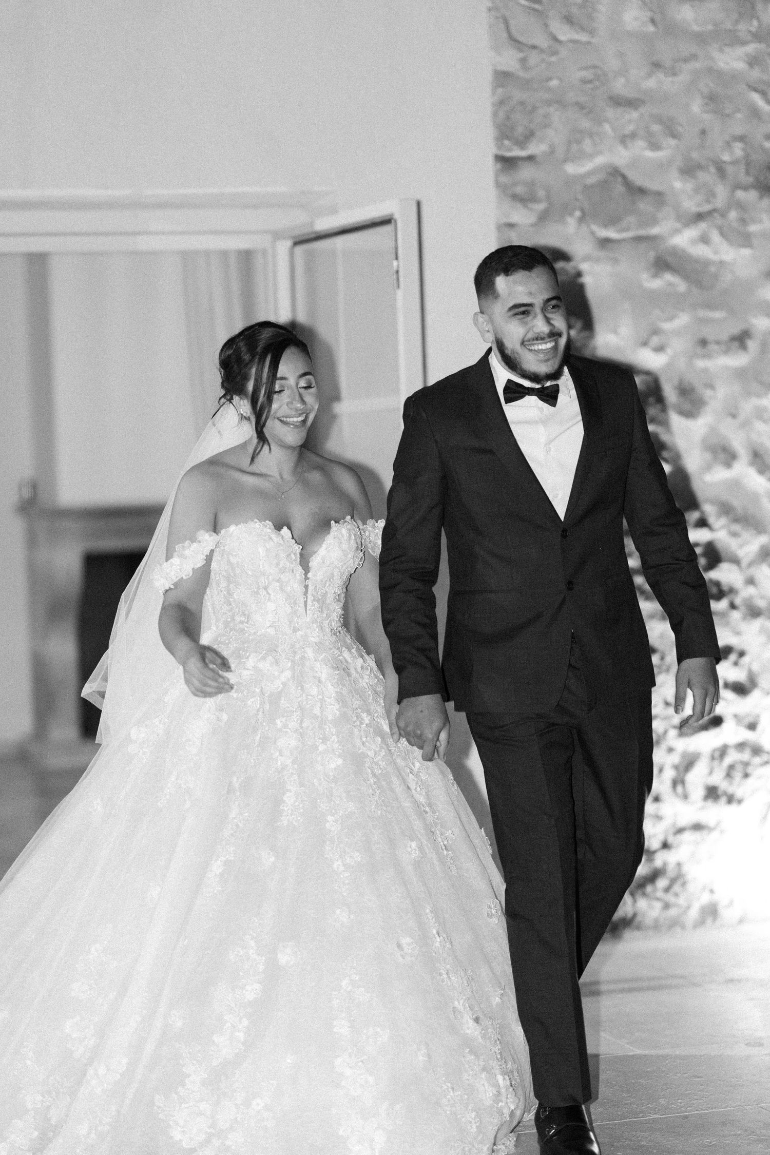 Black and white photo of a smiling bride and groom making a grand entrance at their wedding reception.