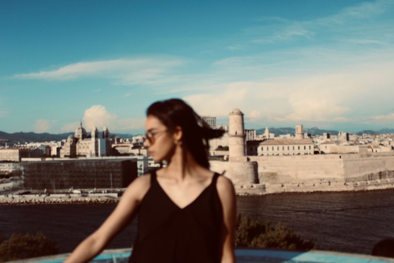 Woman in black top standing with historic Marseille fort and blue sky in the background.