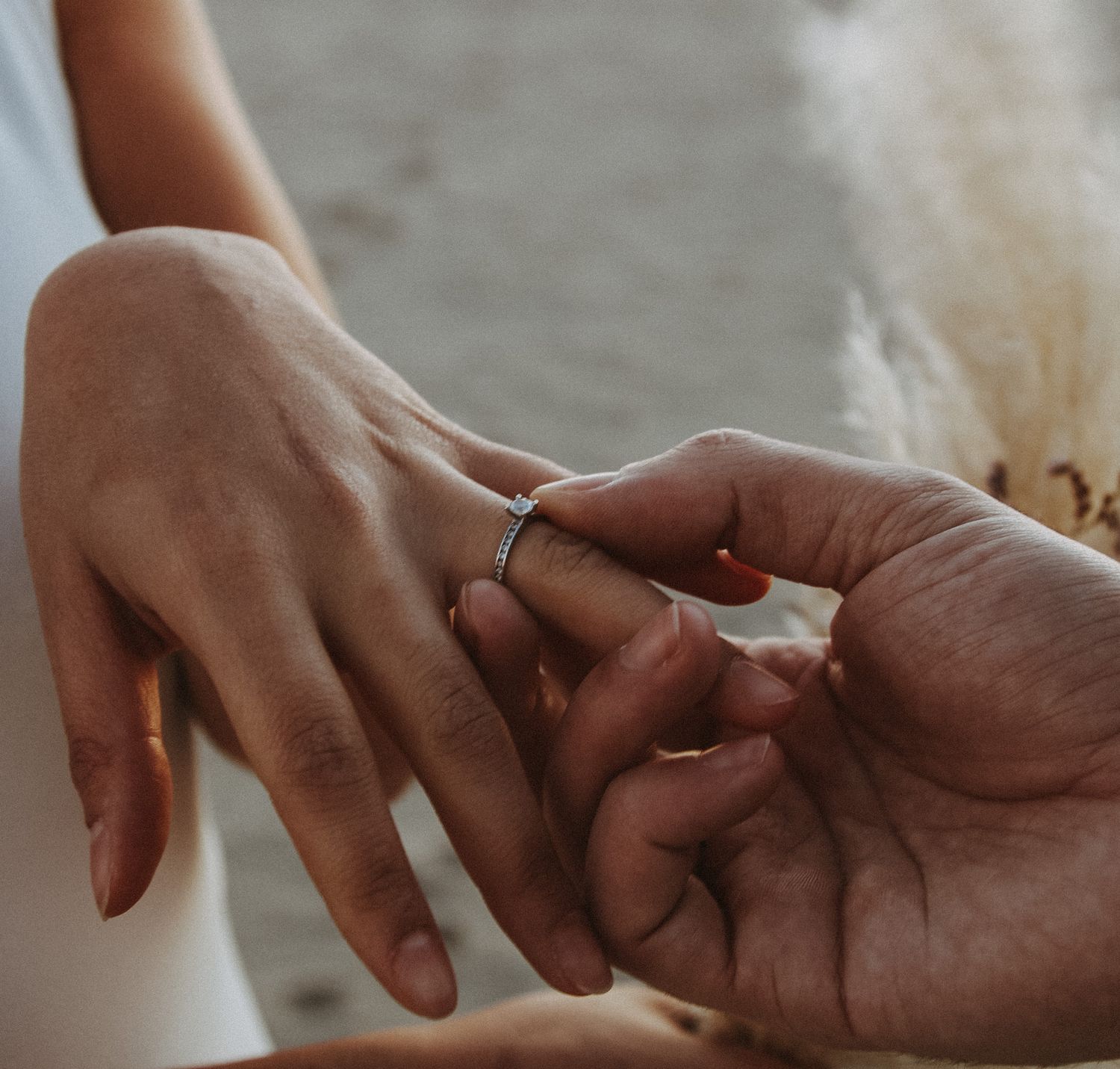 Close-up of a groom sliding a wedding ring onto the bride's finger during an outdoor ceremony.