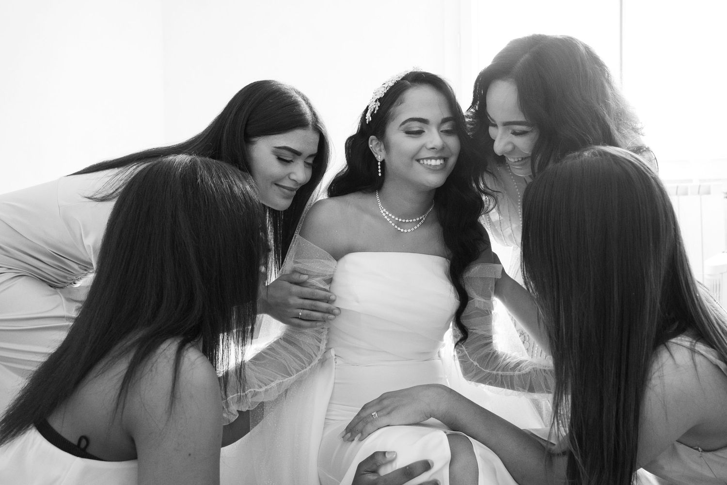 Bride surrounded by bridesmaids in white dresses sharing a joyful moment together before the wedding ceremony.