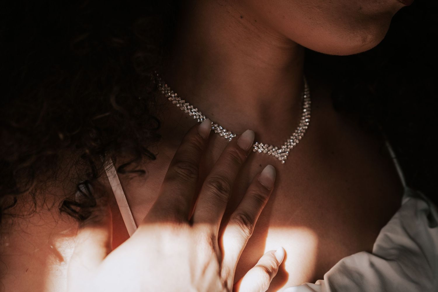 Bride wearing a sparkling diamond choker necklace with light casting a warm glow on her neckline.