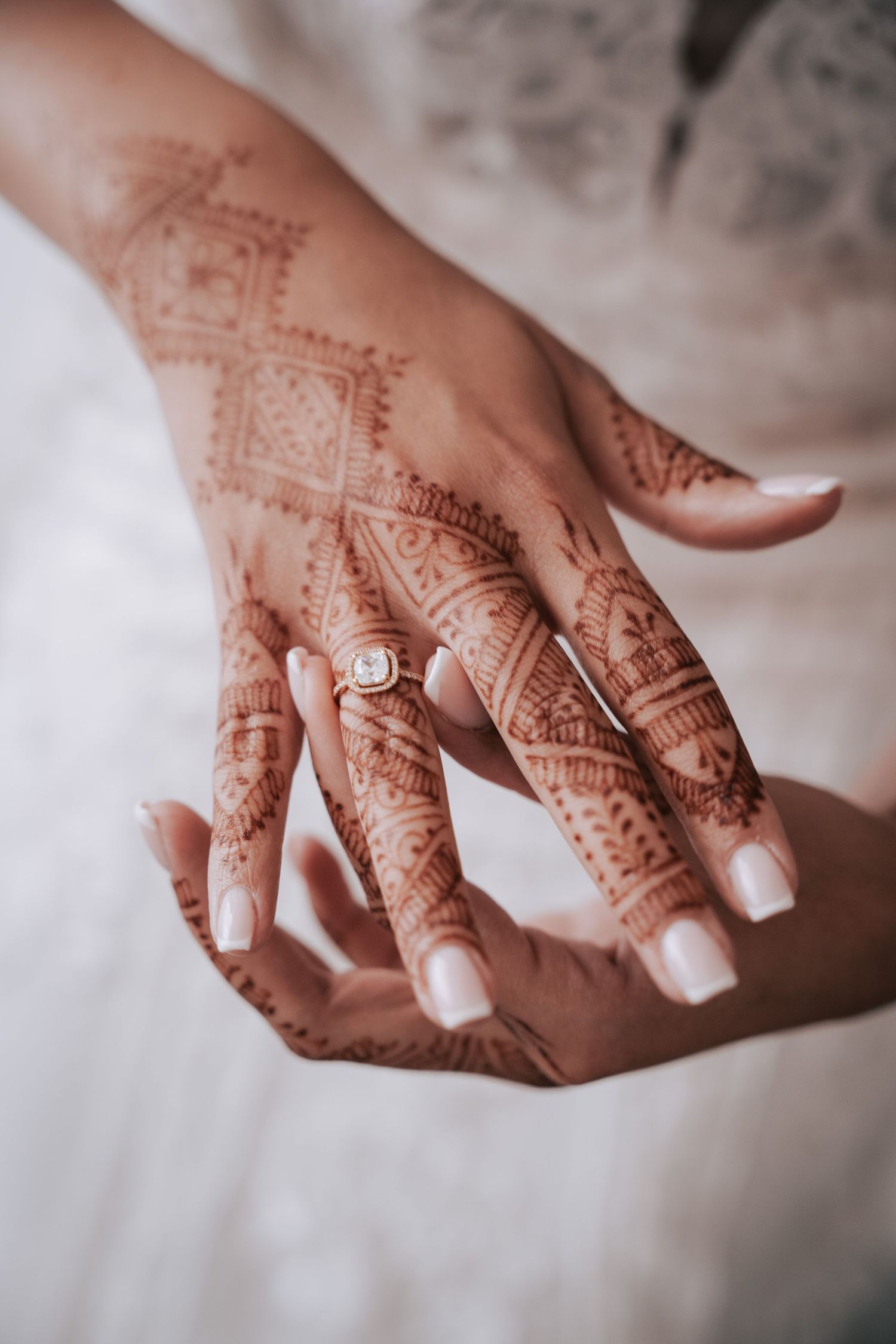 Close-up of bride's hands adorned with intricate henna mehndi design and diamond engagement ring.