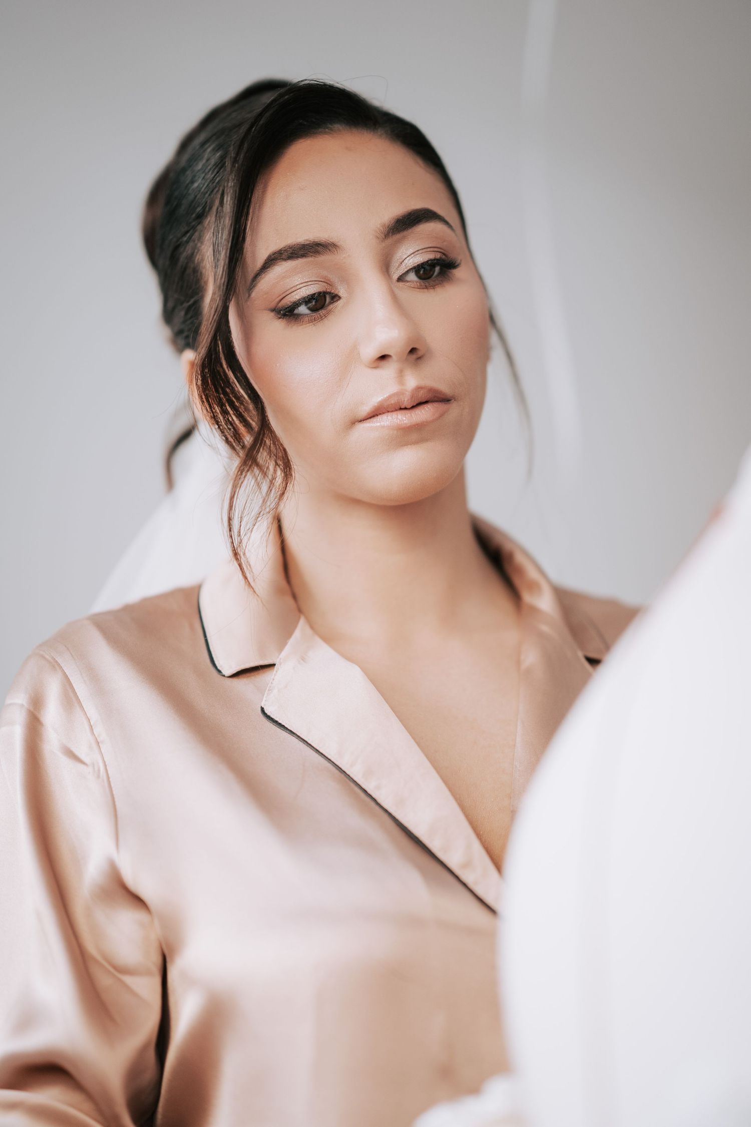 Beautiful bride in a satin robe with natural glam makeup prepares on her wedding day.