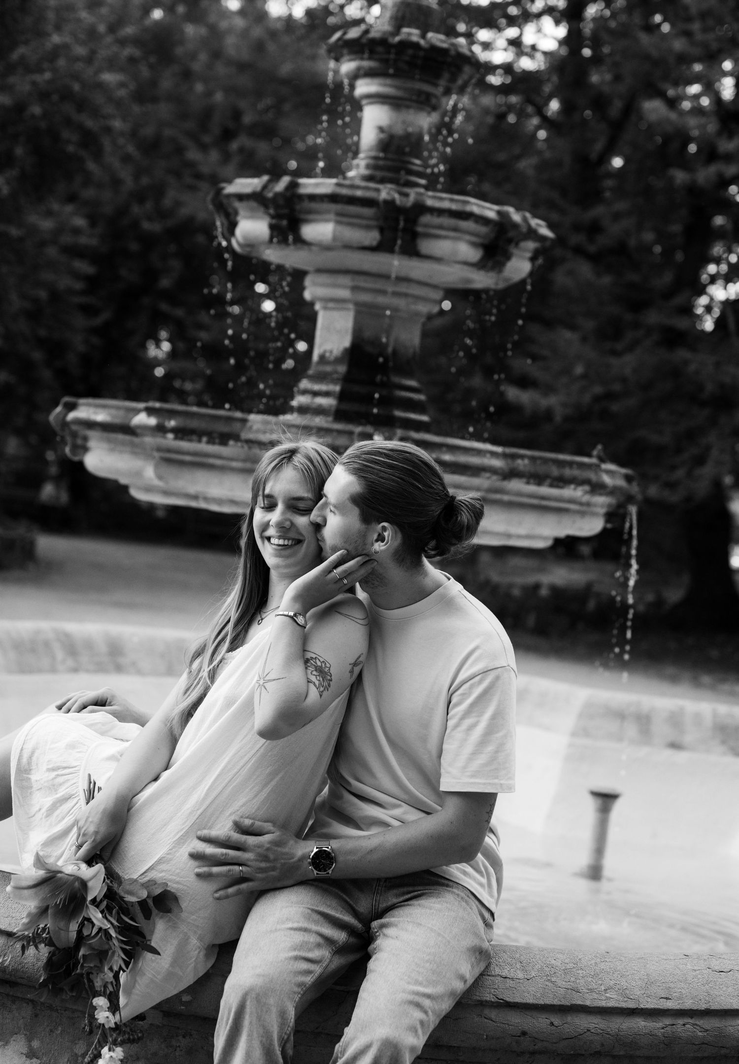 Black and white photo of a couple sitting and embracing by an ornate stone fountain.