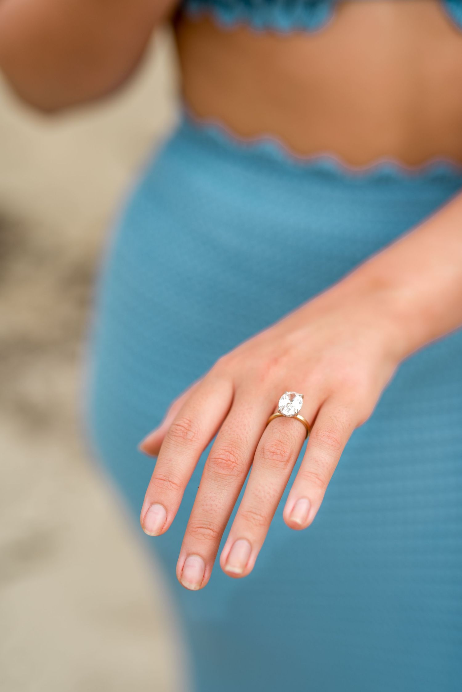 Close-up of oval diamond engagement ring on womans hand against blue knit dress.