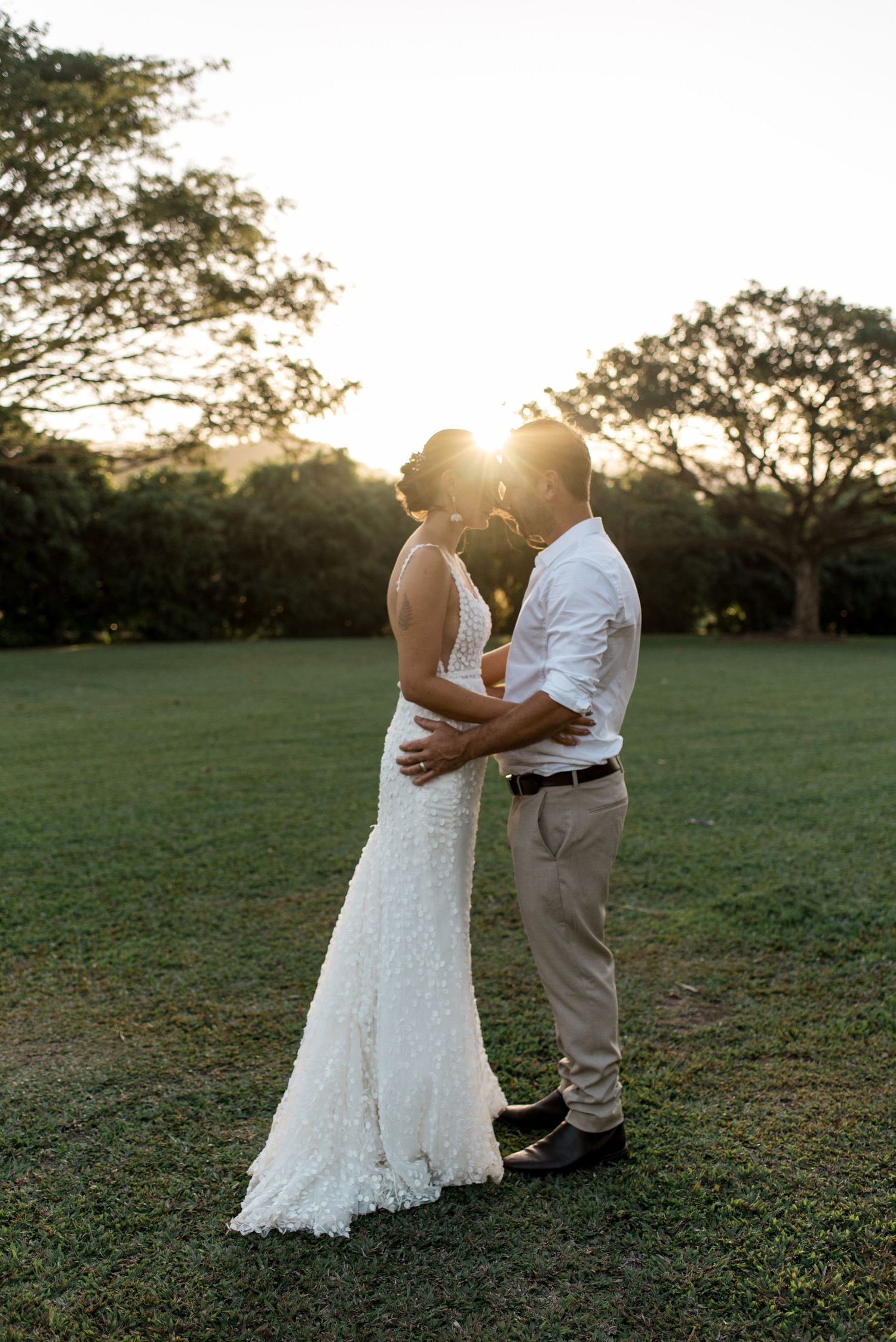 Bride and groom embracing in silhouette against stunning golden sunset in open field.