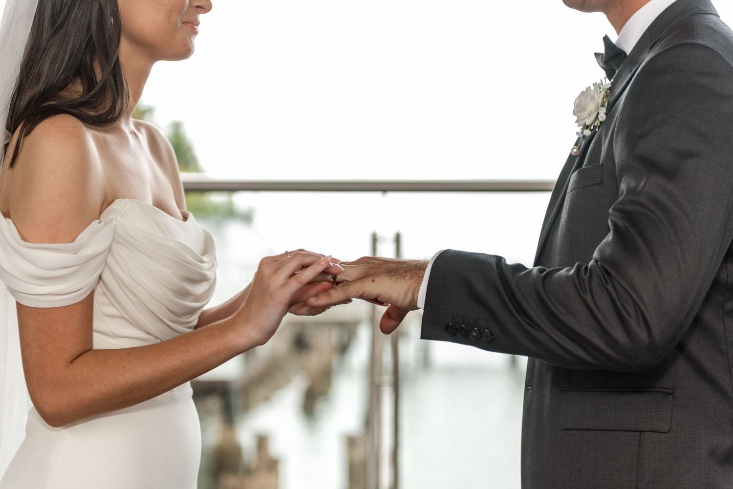 Bride places wedding ring on grooms hand during outdoor waterfront ceremony close-up.