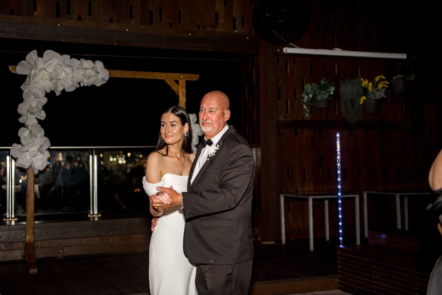 Bride shares a tender father-daughter dance at wedding reception with white balloon arch in background.