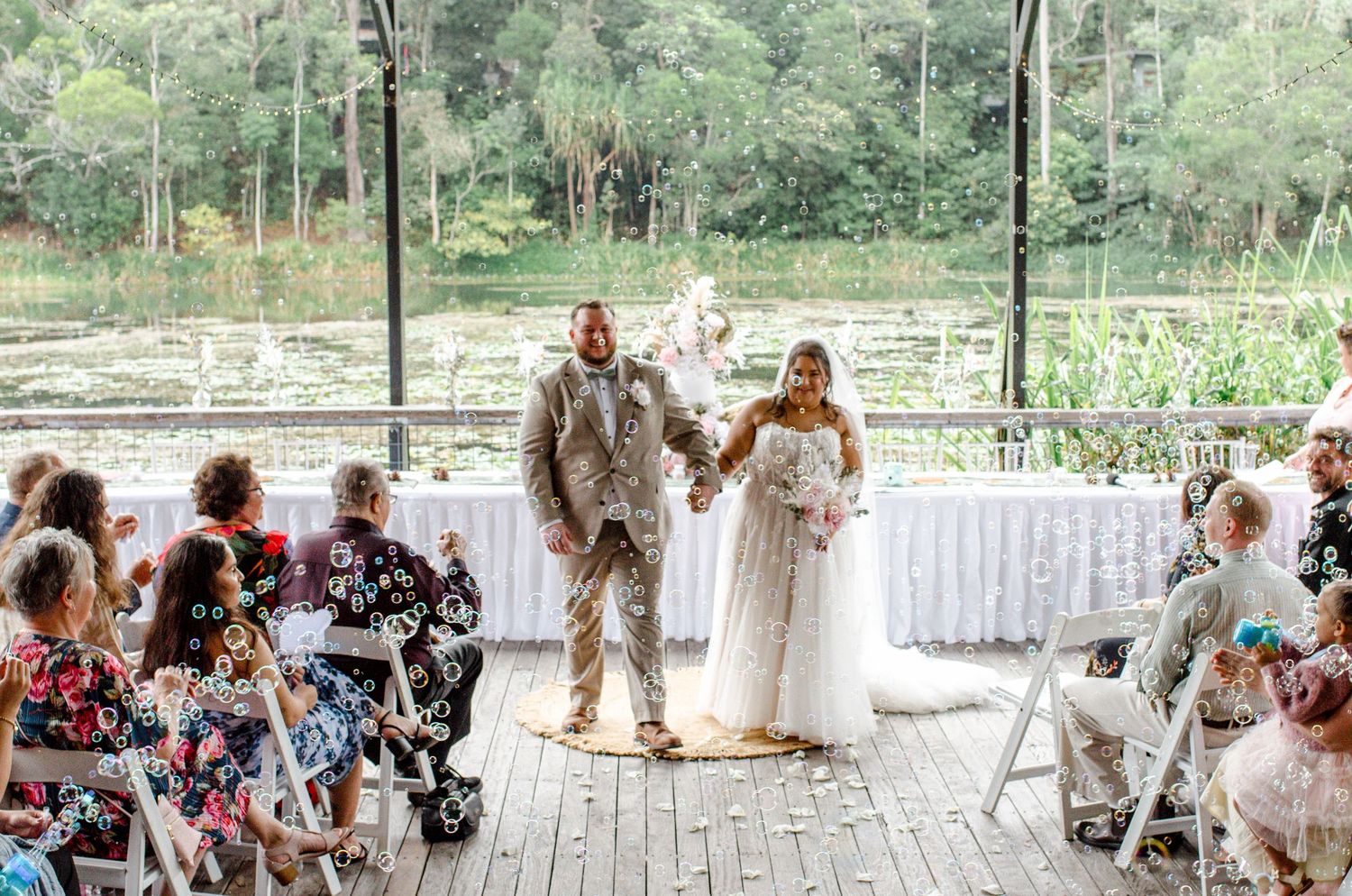 Bride and groom hold hands at the altar during wedding ceremony with guests seated on both sides.