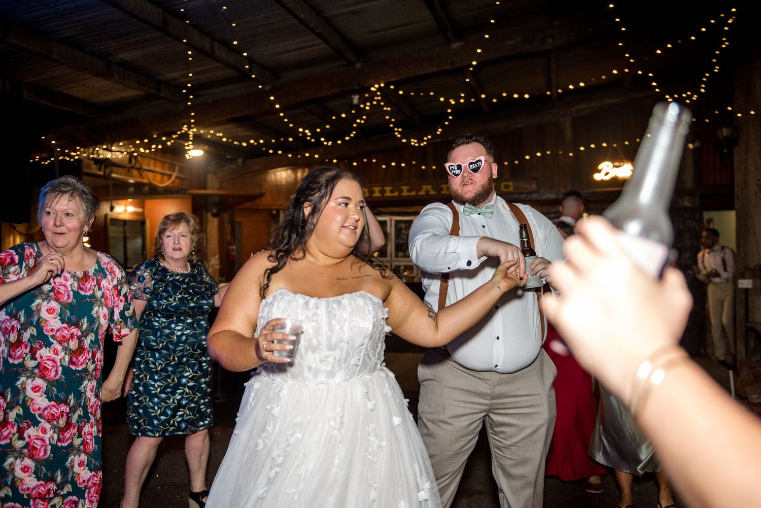 Bride and groom dancing together at festive wedding reception with string lights overhead.
