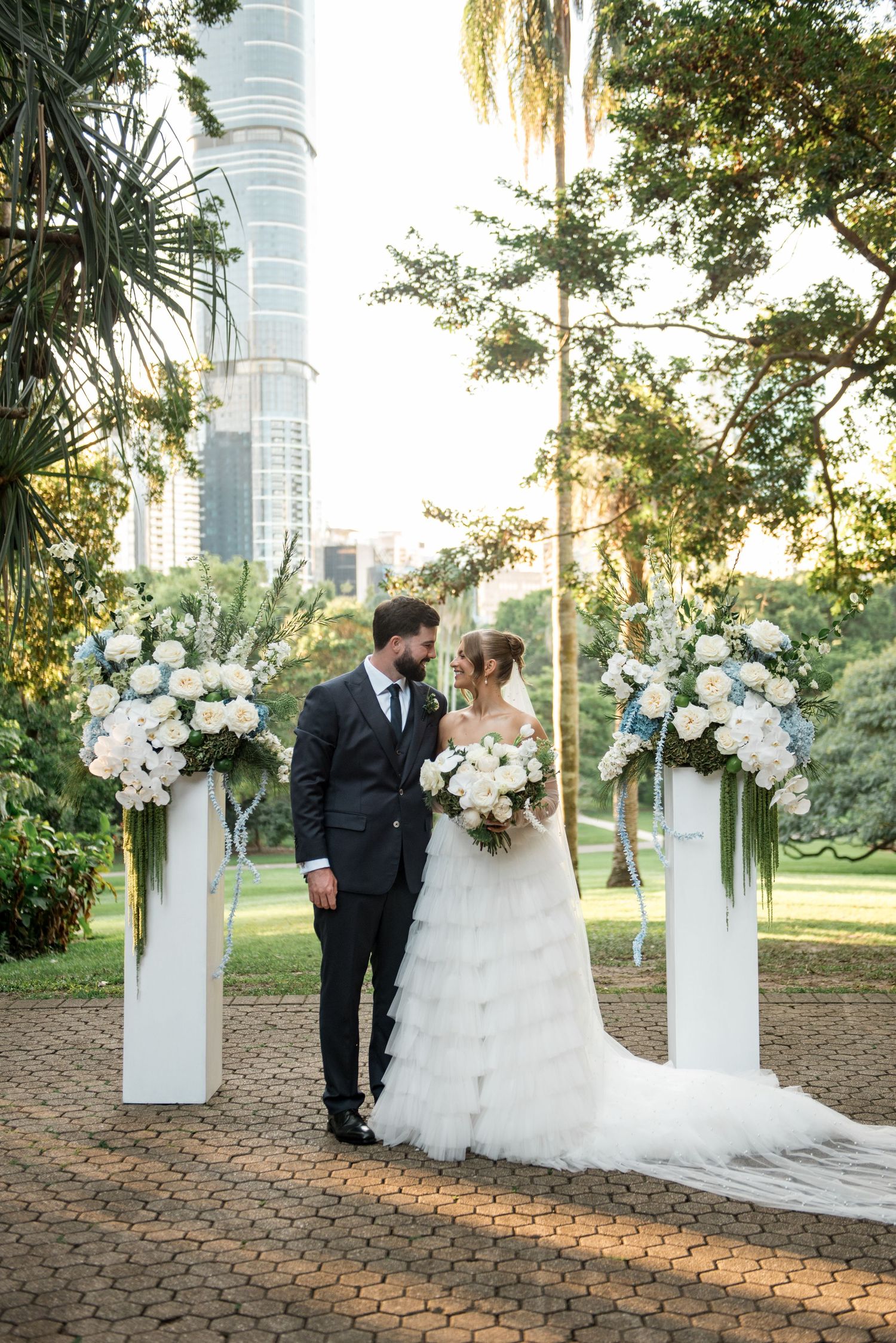 Bride and groom share romantic moment at outdoor wedding altar with white floral pillars.