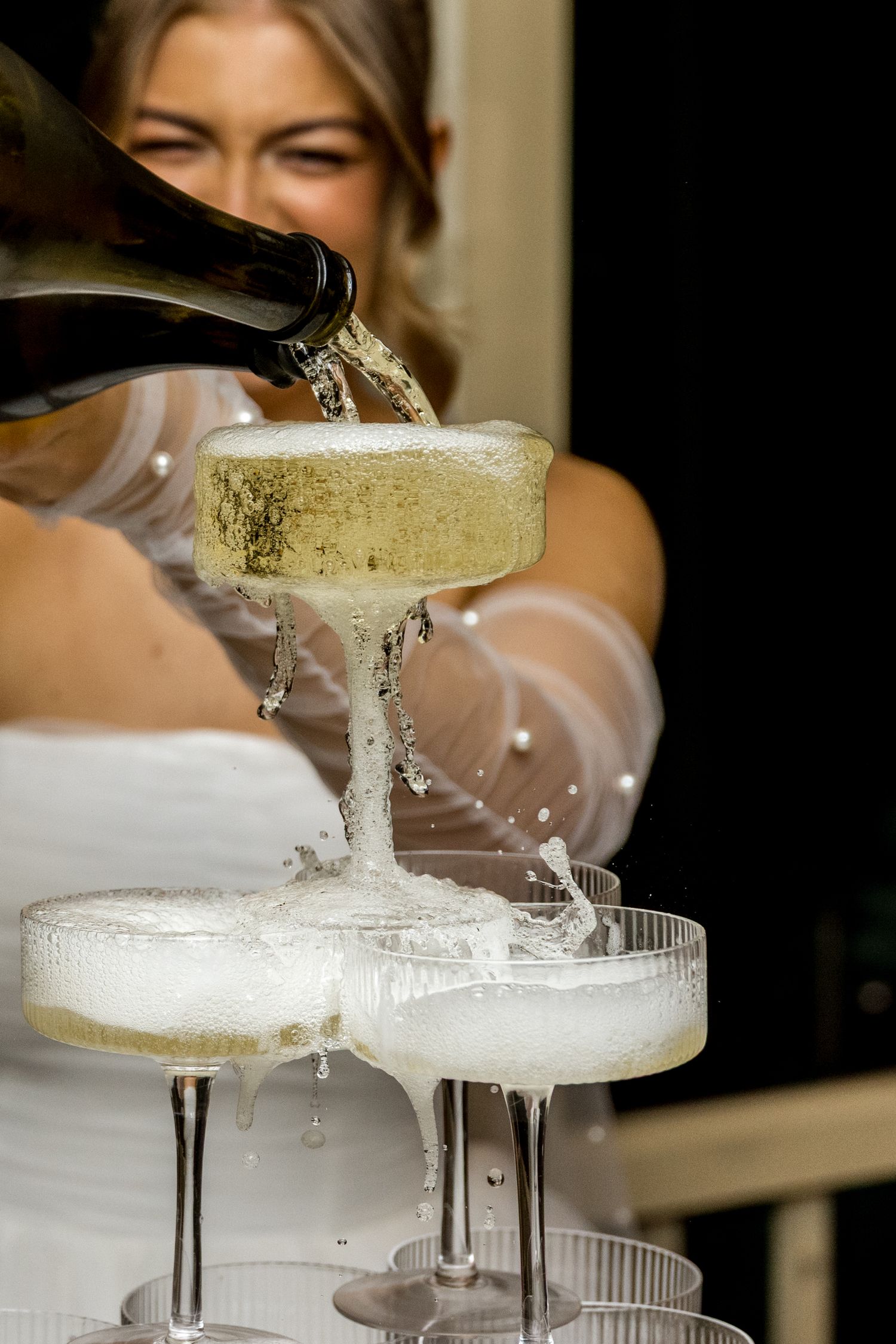 Bride pours champagne into an overflowing wedding champagne tower at reception.