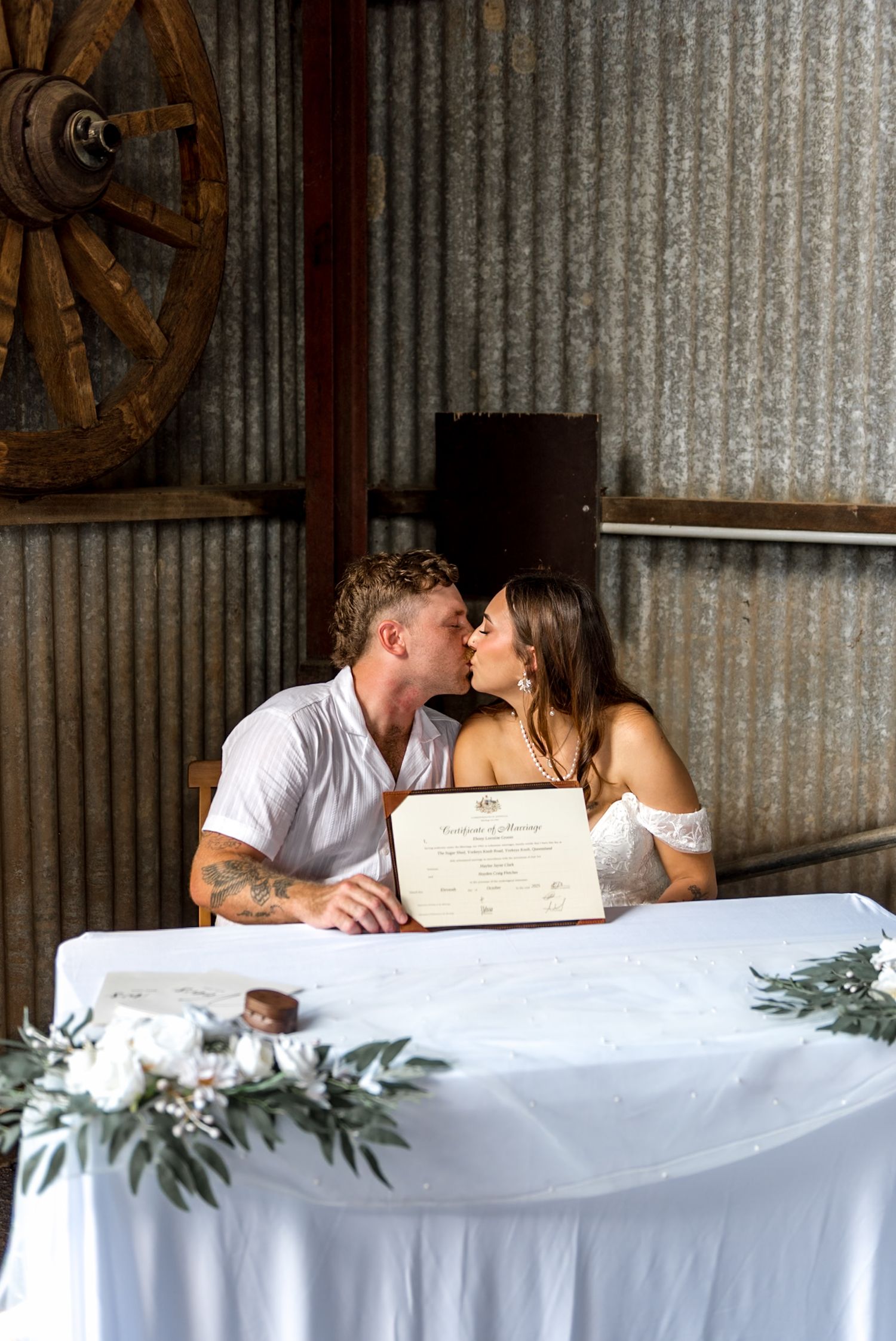 Newlyweds share a kiss while holding their marriage certificate at signing table.
