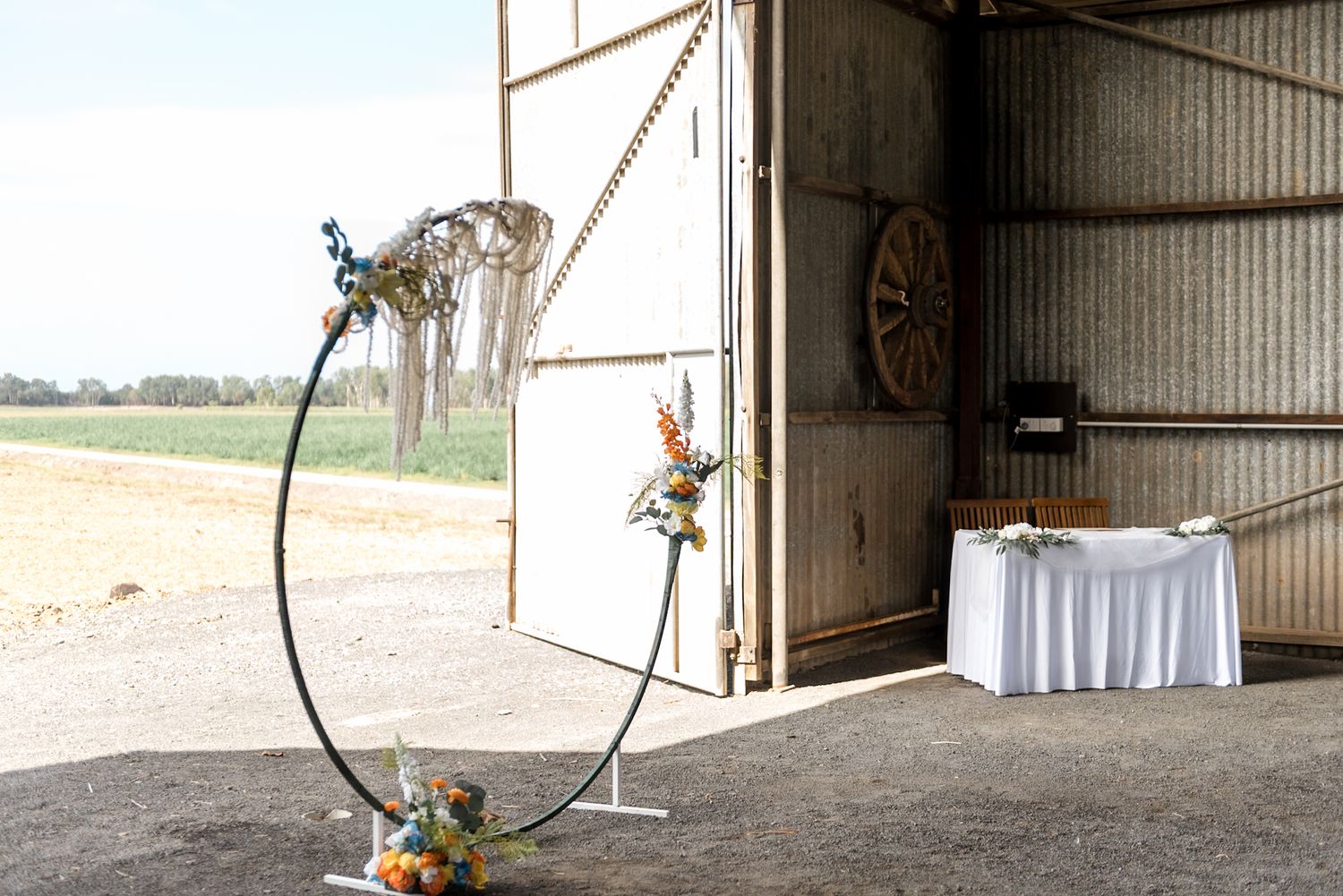 Circular metal wedding arch with macrame and flowers outside a rustic barn venue.