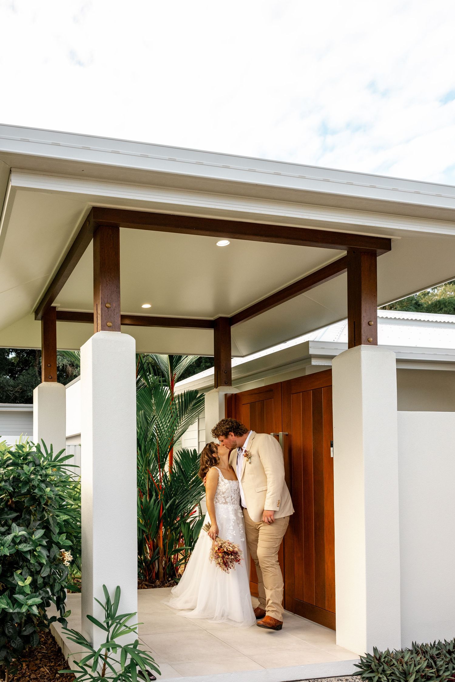 Bride and groom sharing a kiss under a timber pergola at venue entrance.
