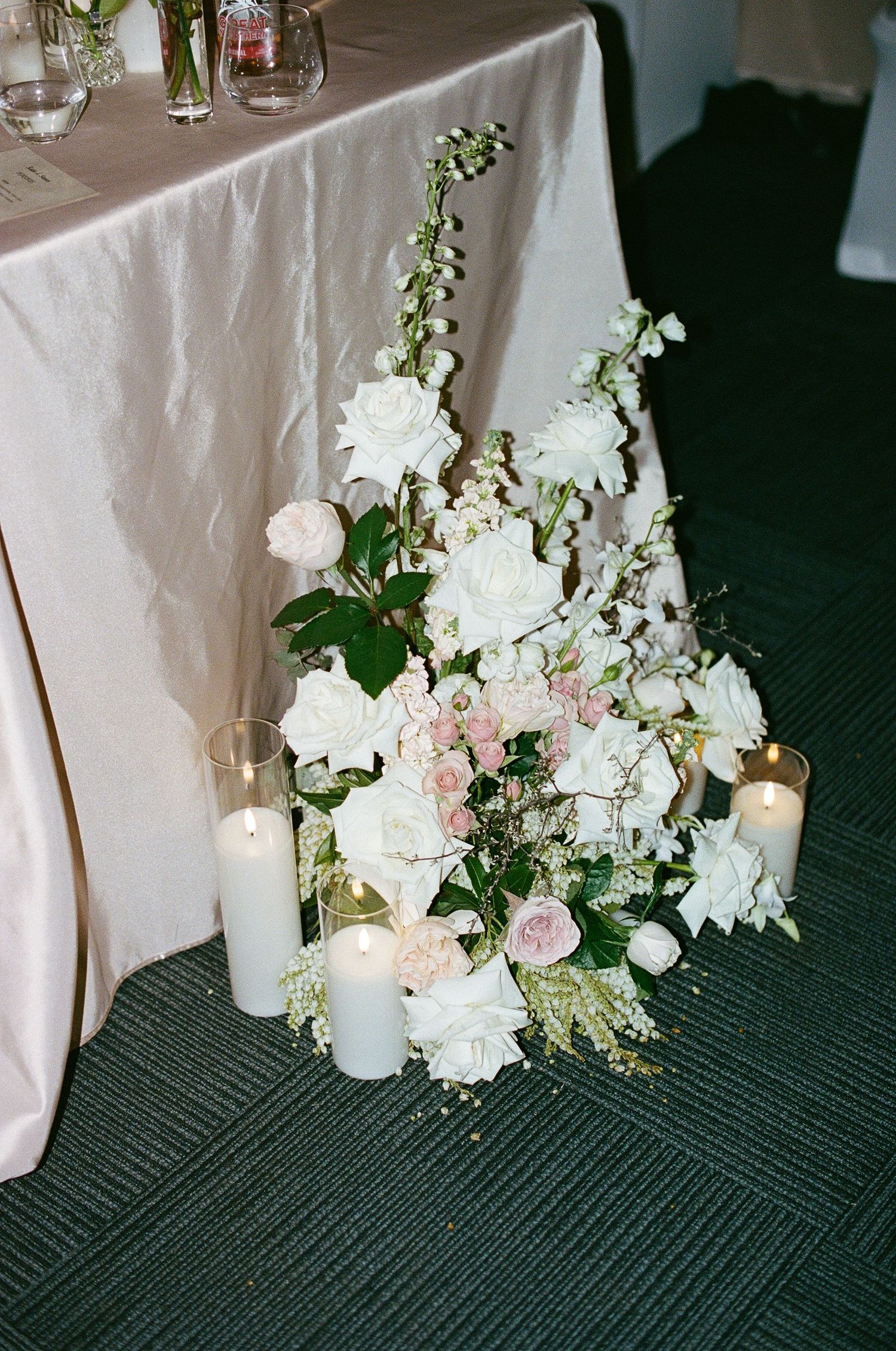 Elegant white and pink floral wedding centerpiece with candles on green carpet.