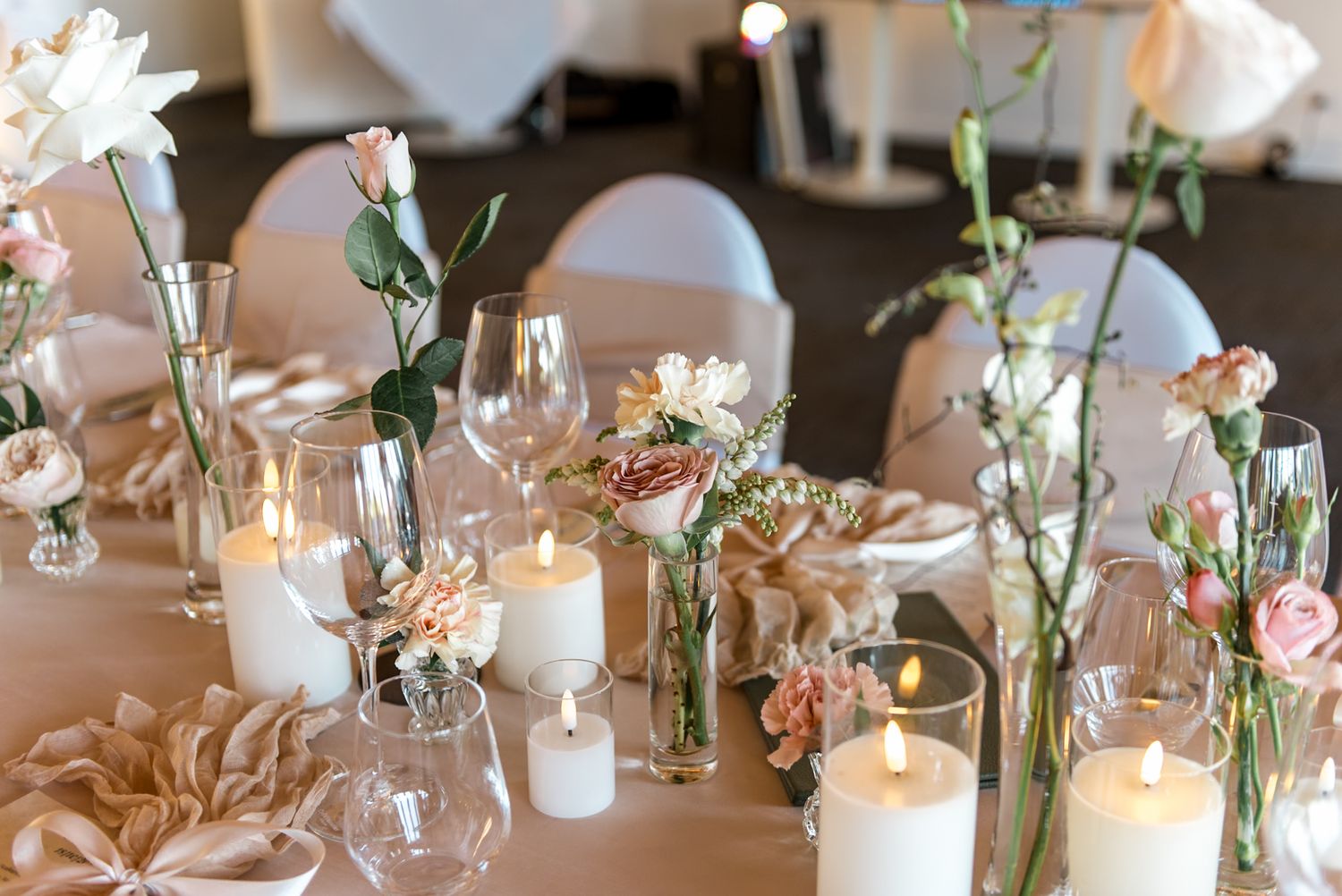 Elegant wedding tablescape featuring white pillar candles, blush roses, crystal glassware, and satin ribbon accents.