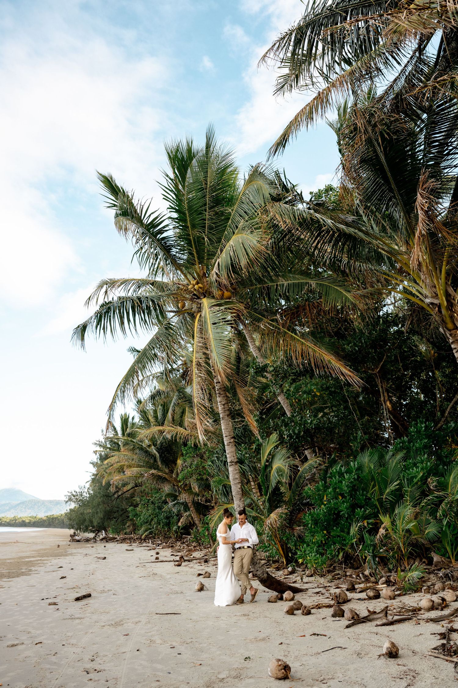 Wedding couple stands together under tall coconut palms on a serene tropical beach at Four Mile Beach, Port Douglas.