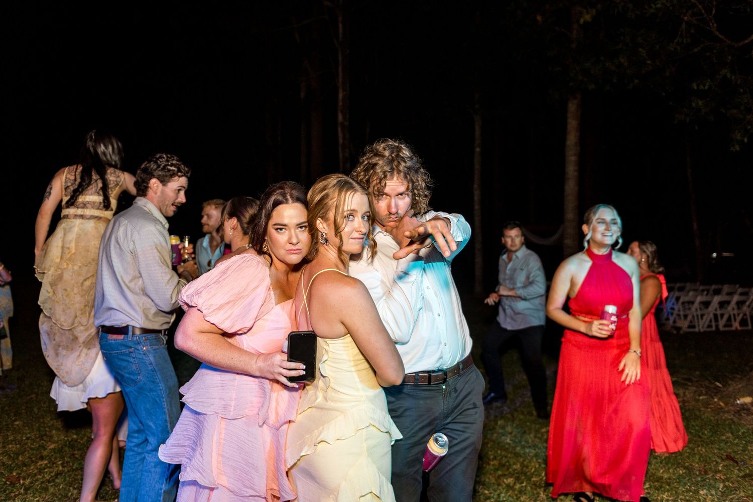 Guests in colorful formal attire dancing and posing at outdoor evening wedding reception.