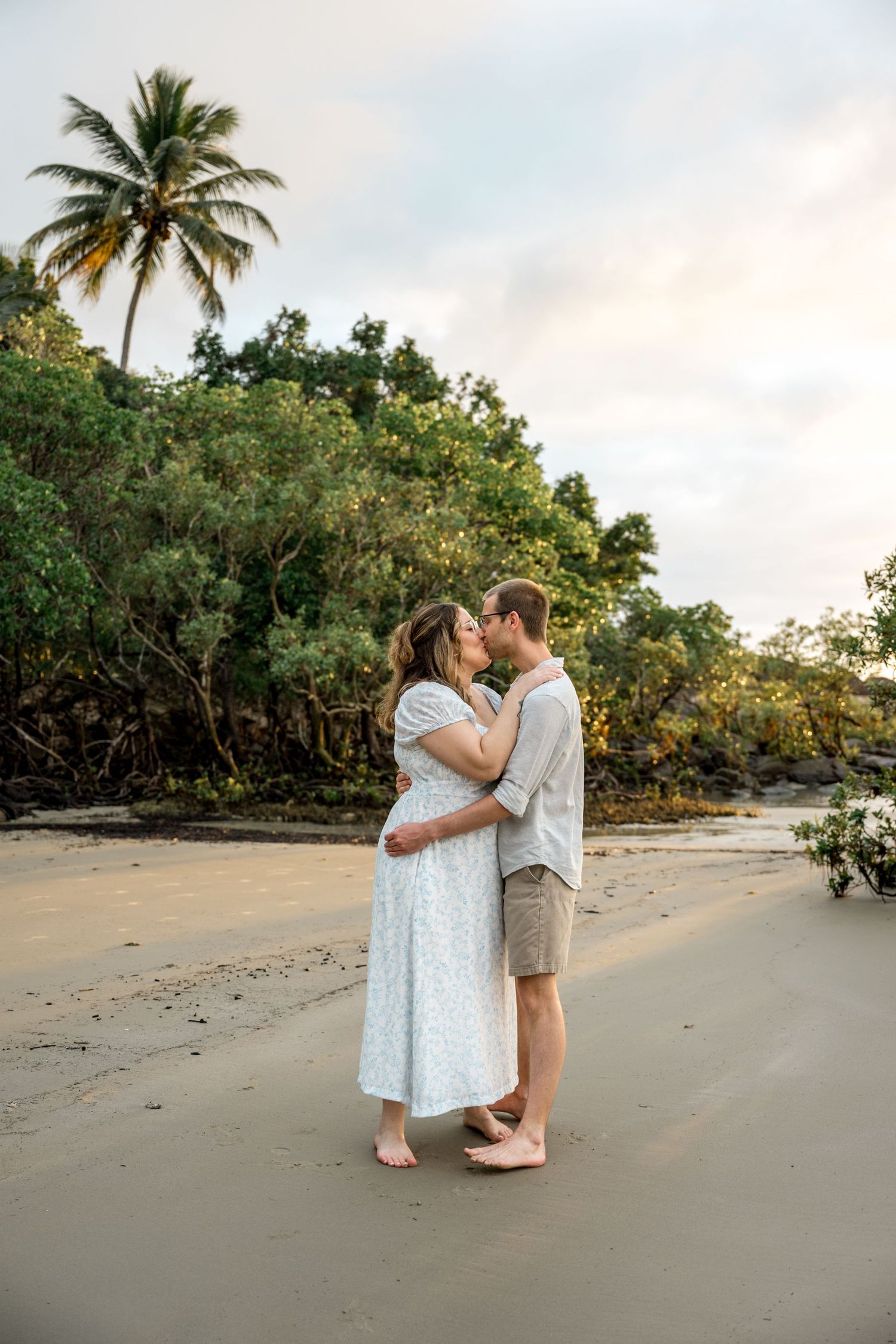 Couple kissing on a sandy tropical beach at sunset with tall palm trees in background at Four Mile Beach, Port Douglas.