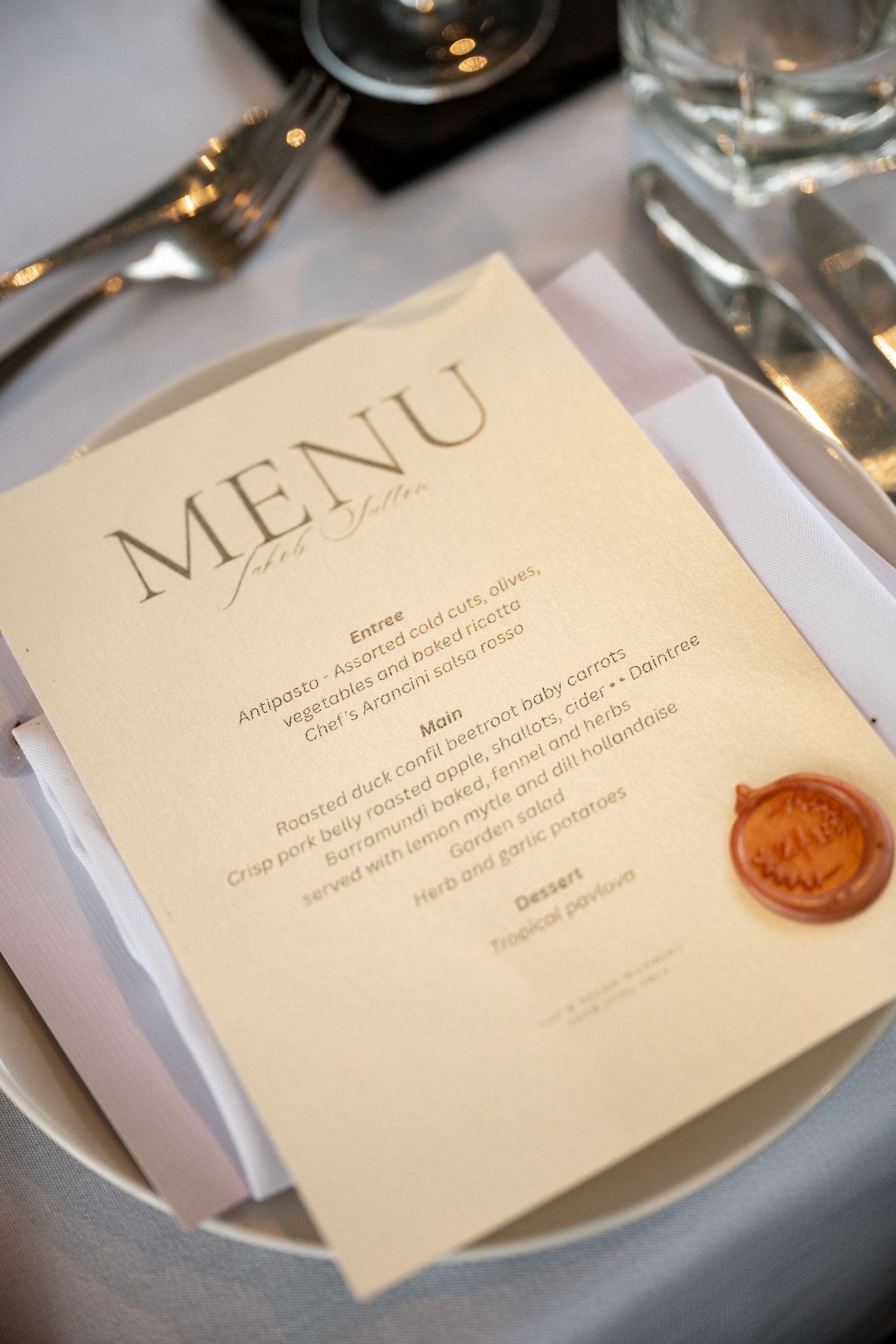Elegant wedding menu card with wax seal on white plate at a formal reception table setting at Sheraton Grand Mirage Port Douglas.