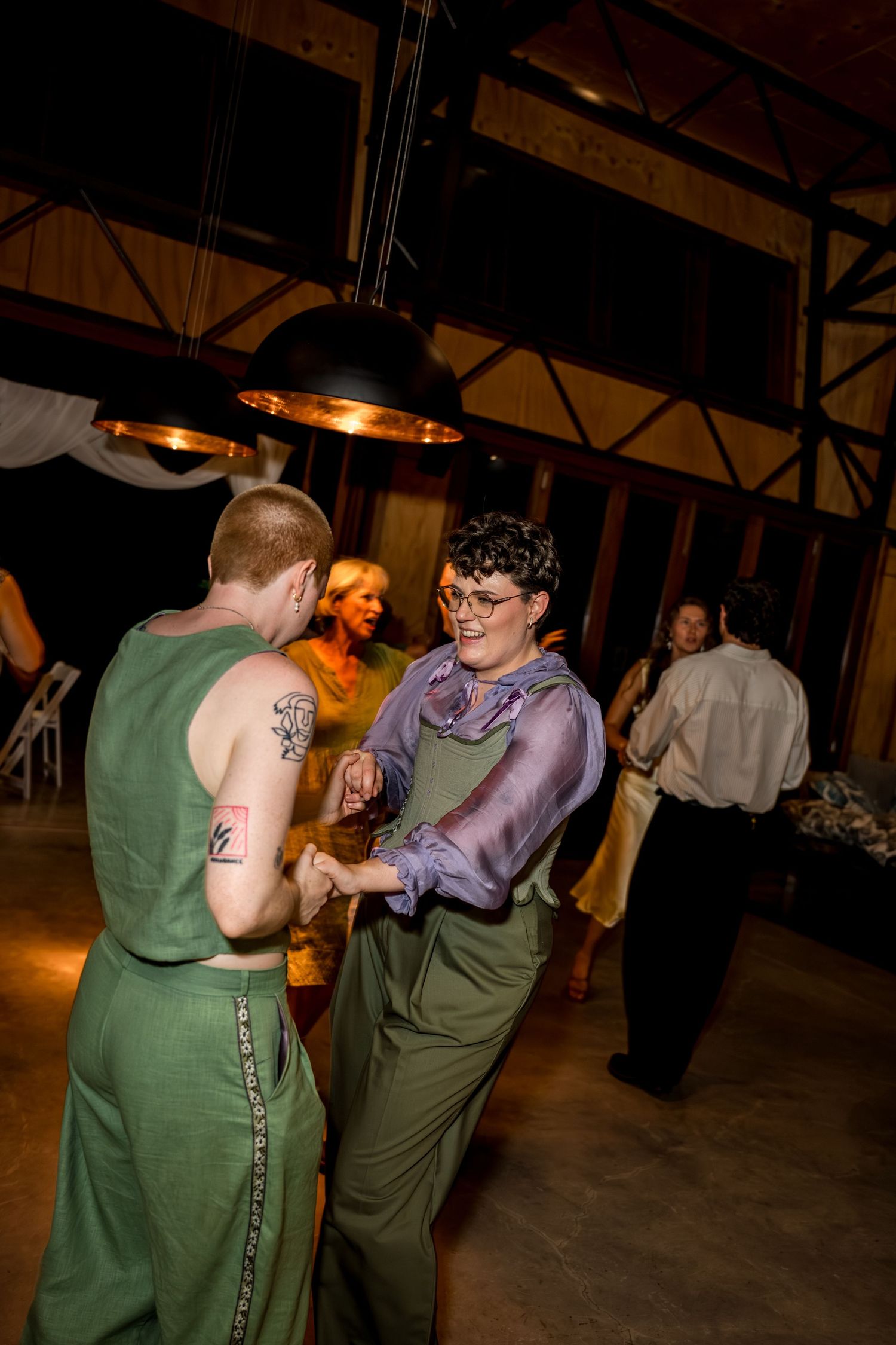 Newlyweds in green outfits laugh and dance joyfully at their wedding reception.