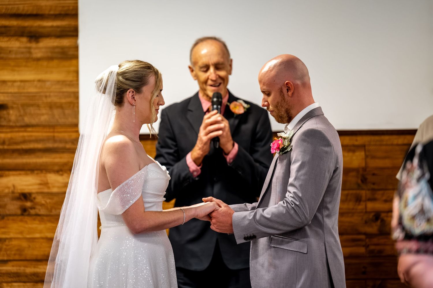 Bride and groom exchange vows holding hands while officiant reads during intimate wedding ceremony.