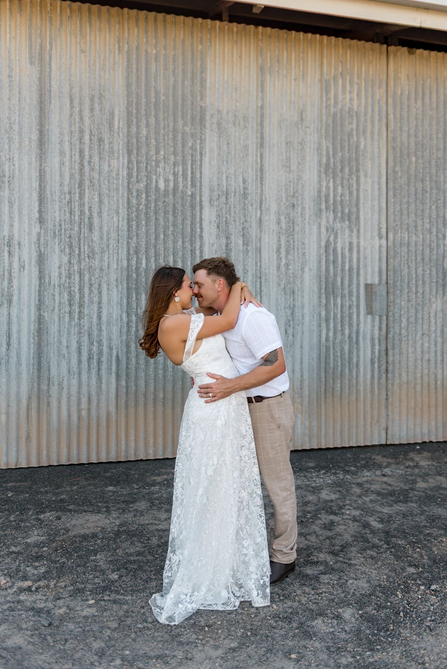 Bride and groom share a romantic kiss while embracing in front of a rustic corrugated metal wall.