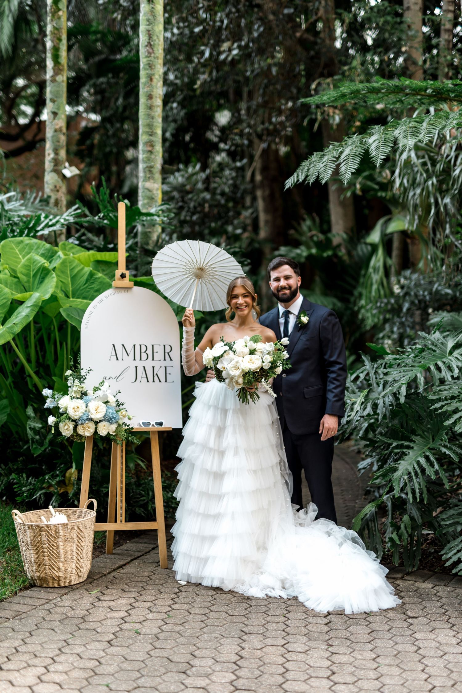 Bride and groom pose beside personalized Amber and Jake wedding welcome sign in garden.