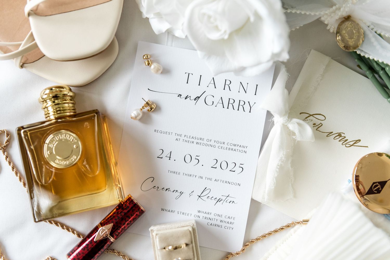 Wedding flat lay featuring invitation for Tiarni and Garry dated 24.05.2025, perfume, jewelry and accessories.