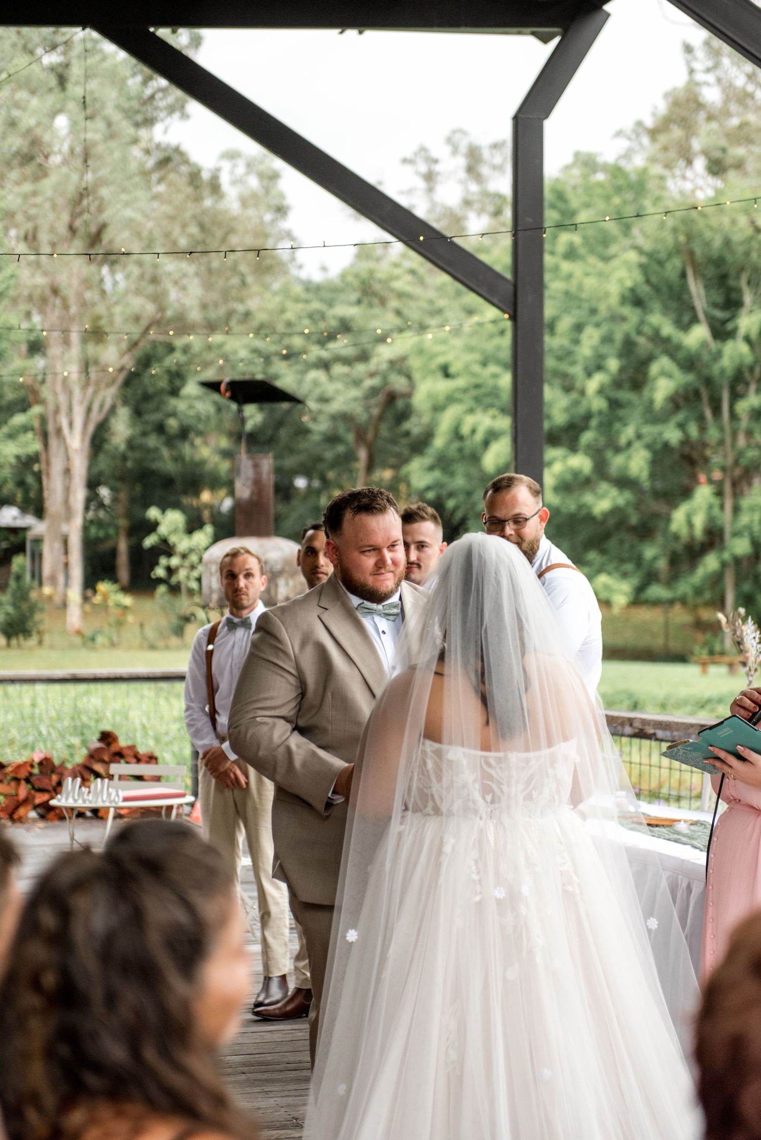 Groom gazes at bride during outdoor wedding vows with groomsmen standing behind them.