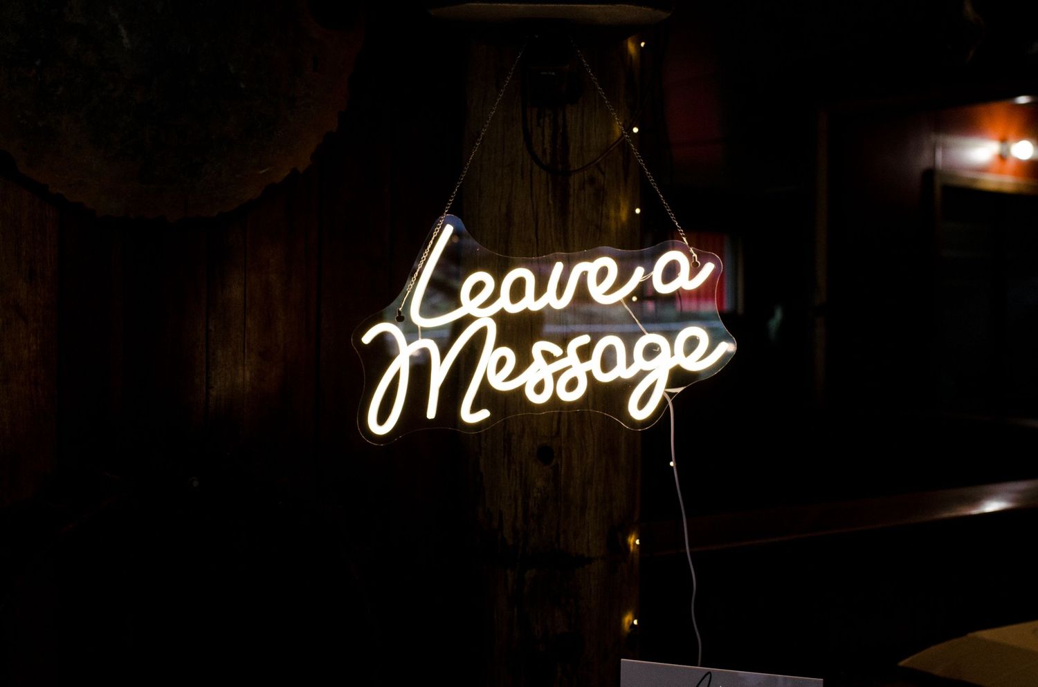 Glowing neon Leave a Message sign hanging in a dark rustic wooden wedding venue.